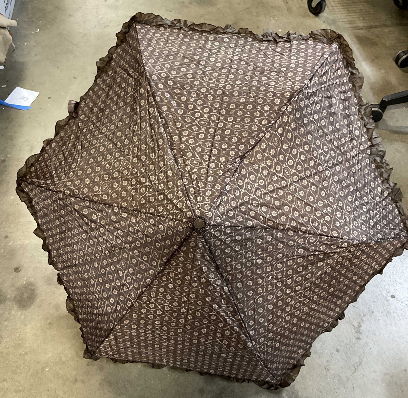 Sabon Brown Ruffled Parasol: Sabon brown ruffled parasol. Comes with protective cover. U shaped handle. Ruffled trim and geometric pattern. Measures approx 25 x 32 inches, when extended. Surface wear consistent with exposure.