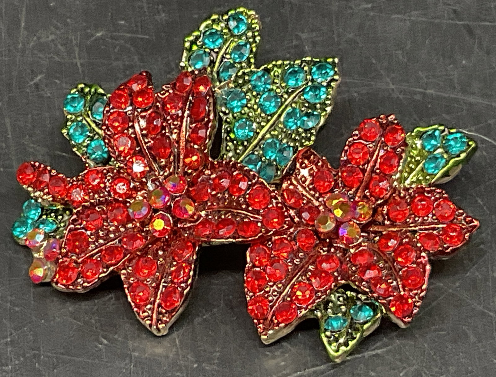 Double Poinsettia Rhinestone Brooch: Double Poinsettia Flowers Brooch. Red, Orange, and Green Rhinestone Accents. Gold-Toned Backing. Missing Stone. No Visible Markings or Brand. Measures app 1.75in H x 1.5in W. Poinsettias, Flowers,