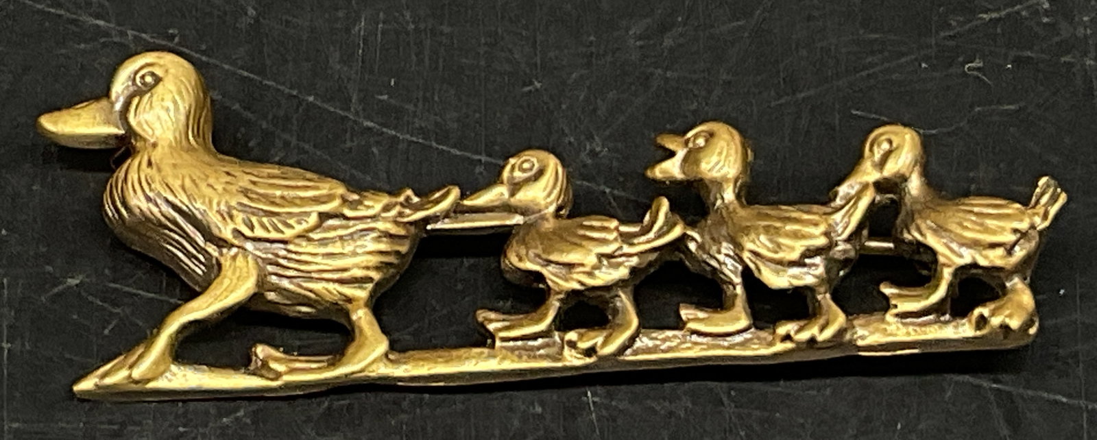 VTG Brass-Toned Mother Duck&Ducklings Brooch: Vintage Brass-Toned Mother Duck and Ducklings Brooch. Textured Feathers. Trademark on the Back and Triangle Shaped Makers Mark. Condition Consistent With Exposure. Measures app 0.5in H x 2in L.