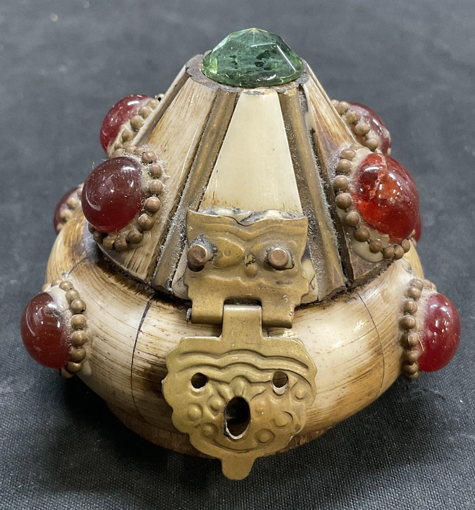 VINTAGE Tibetan Bone Stone Inlay Trinket Box: Vintage Tibetan Trinket Box. Bone Tiles on Brass Frame. Swirled Red Stone Inlay. Green Gem Finial on Cone-Shaped Lid. Brass Hinge. Brown Velvet Interior. Wooden Base. Condition Consistent With Exposur