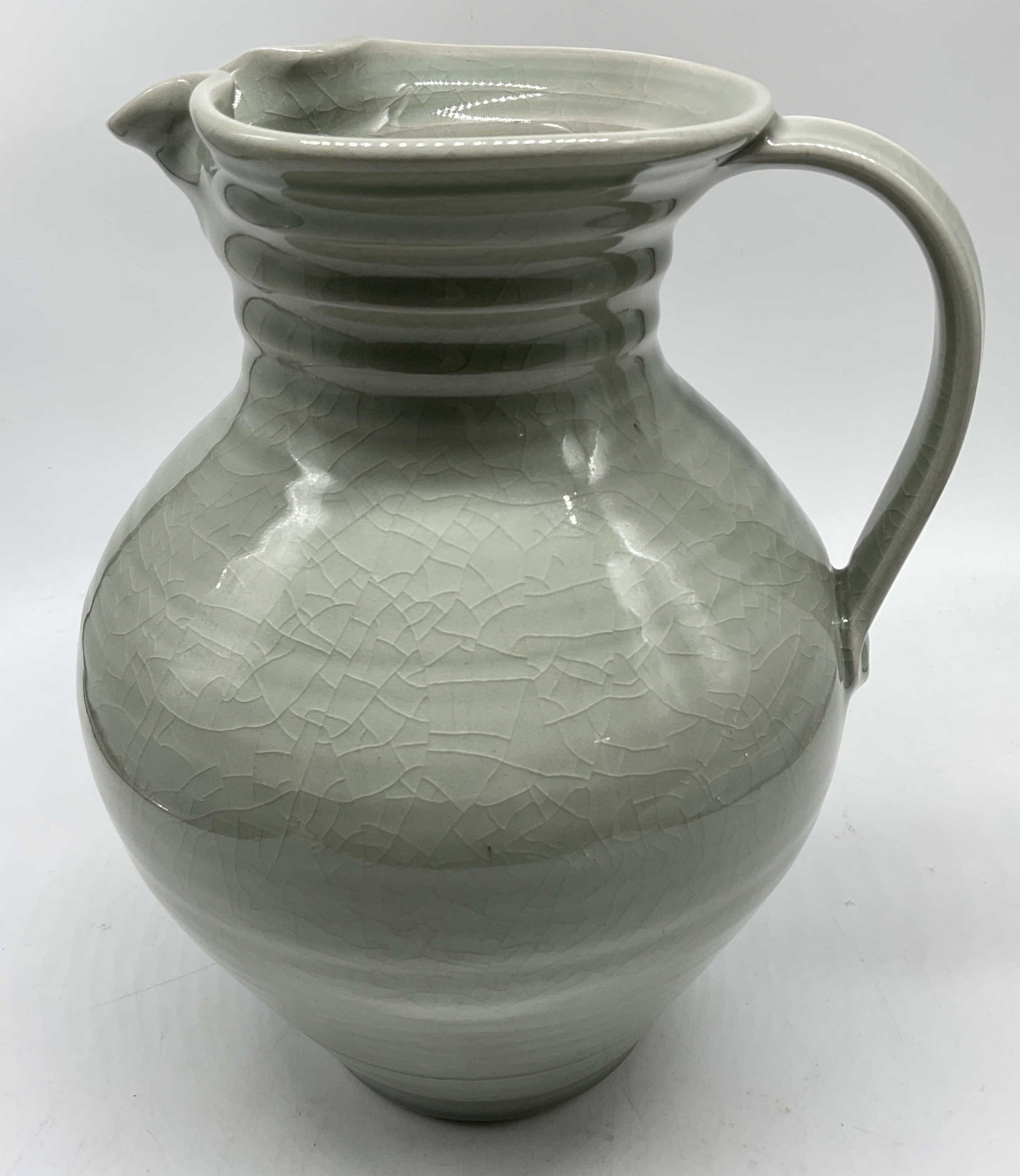 Wavy Rim Crackle Glaze Pottery Pitcher: Wavy Rim Pale Green and Grey Crackle Glaze Pottery Pitcher. Makers Mark on Base. Condition Consistent With Exposure. Measures app 10.5in H x 7.5in Diam. Wavy Rim, Green, Grey, Crackle Glaze, Pottery,
