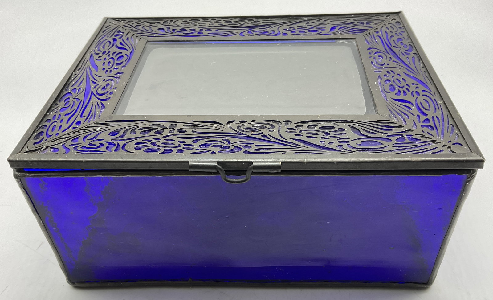 VTG Cobalt Blue Stained Glass Photo Jewelry Box: Vintage Cobalt Blue Stained Glass Jewelry Box. Scrolled Floral Design Metal Filigree Frame with Glass Photo Insert on Lid. Lid Supported by Metal Chain. Aging to Metal Present. Measures app 3.25in H x