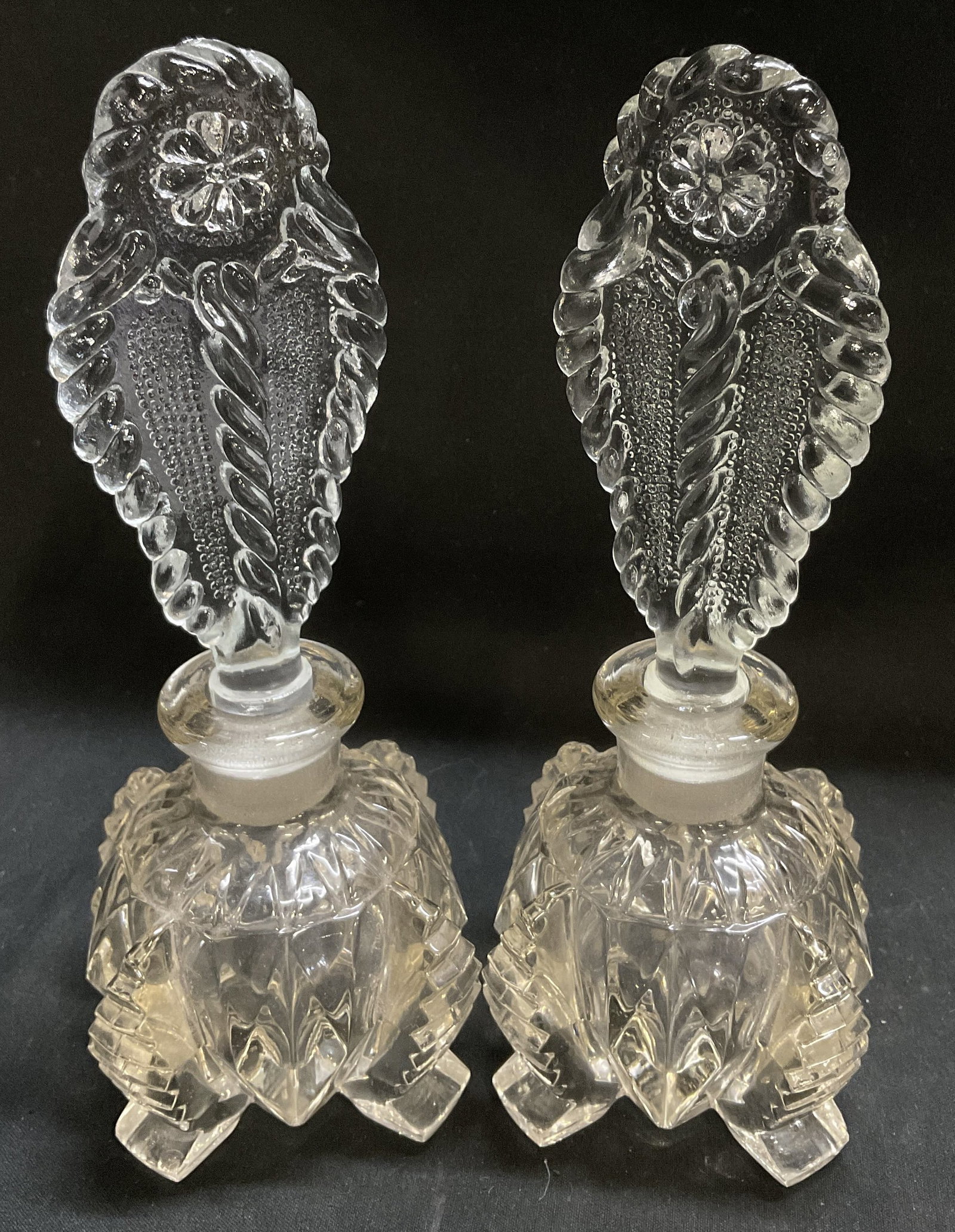 Lt2 VTG Art Deco Pressed Glass Perfume Bottles: 2 Vintage Circa 1930s-1940s Art Deco Style Pressed Glass Perfume Bottles. Large Decorative Flat Stoppers with Floral Motifs. Twisted Pattern on Footed Body. Some Chips on Rim. Measures app 7.5in H x 2