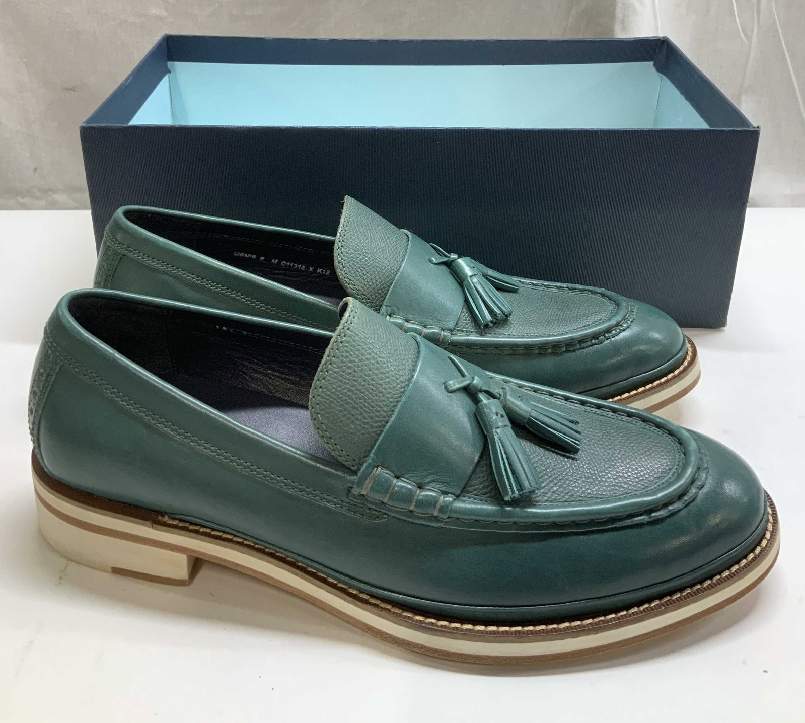 Cole Haan Green Tassel Loafers: Cole Haan green loafers feature a tassel accent at front. Interior is navy toned. Leather. Comes with a box. Size Mens 9. Surface wear consistent to age, use & exposure. Cole Haan green tassel loafers