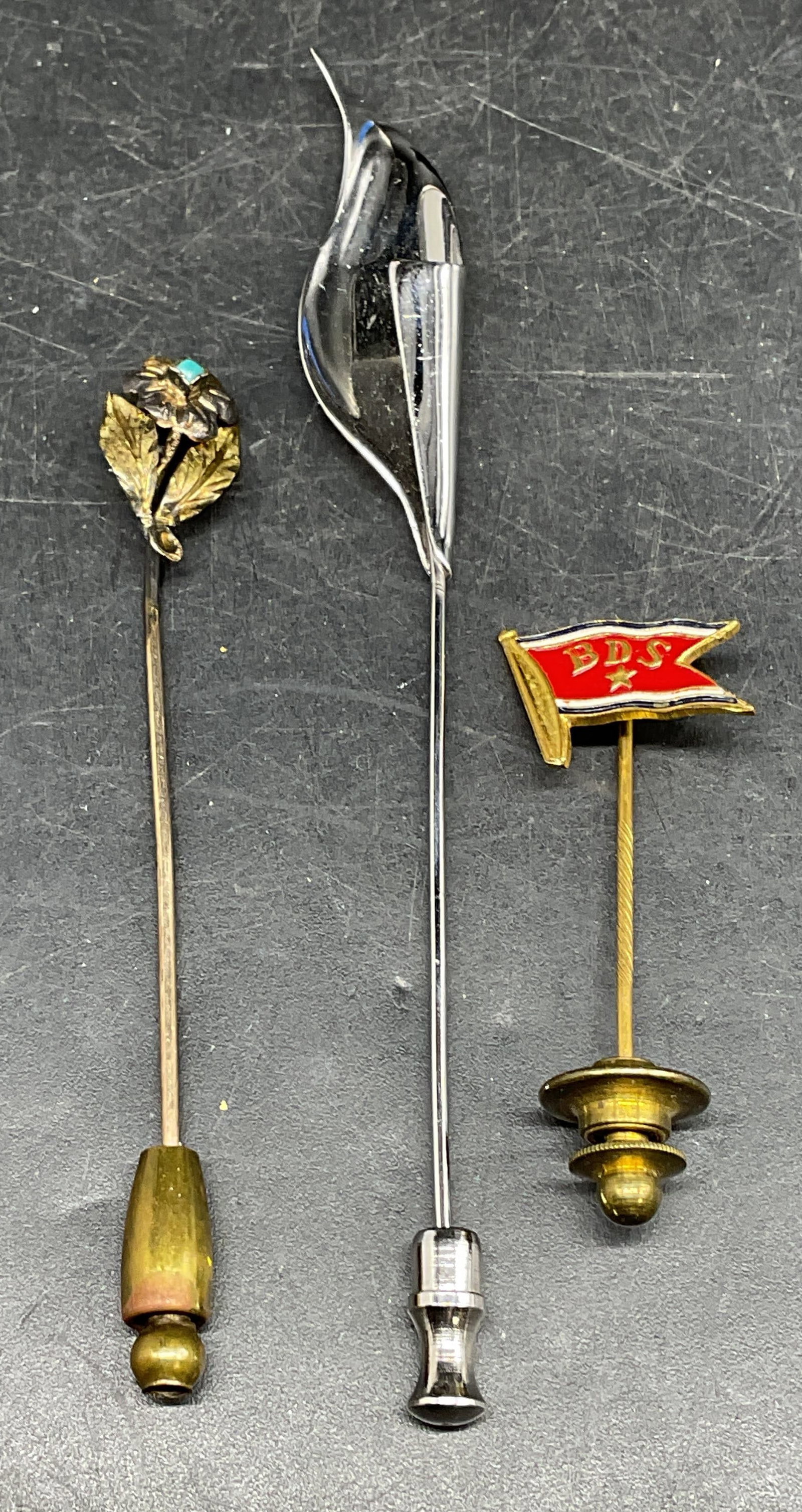 Lot 3 Sterling Silver & Gold Tone Stick Pins: Lot of 3 vintage stick pins. Sterling silver flower stick pin. Marked sterling. Total weight 2.4 grans. Gold tone enamel flag stick pin, reads BDS. Gold tone flower stick pin. Longest measures approx.