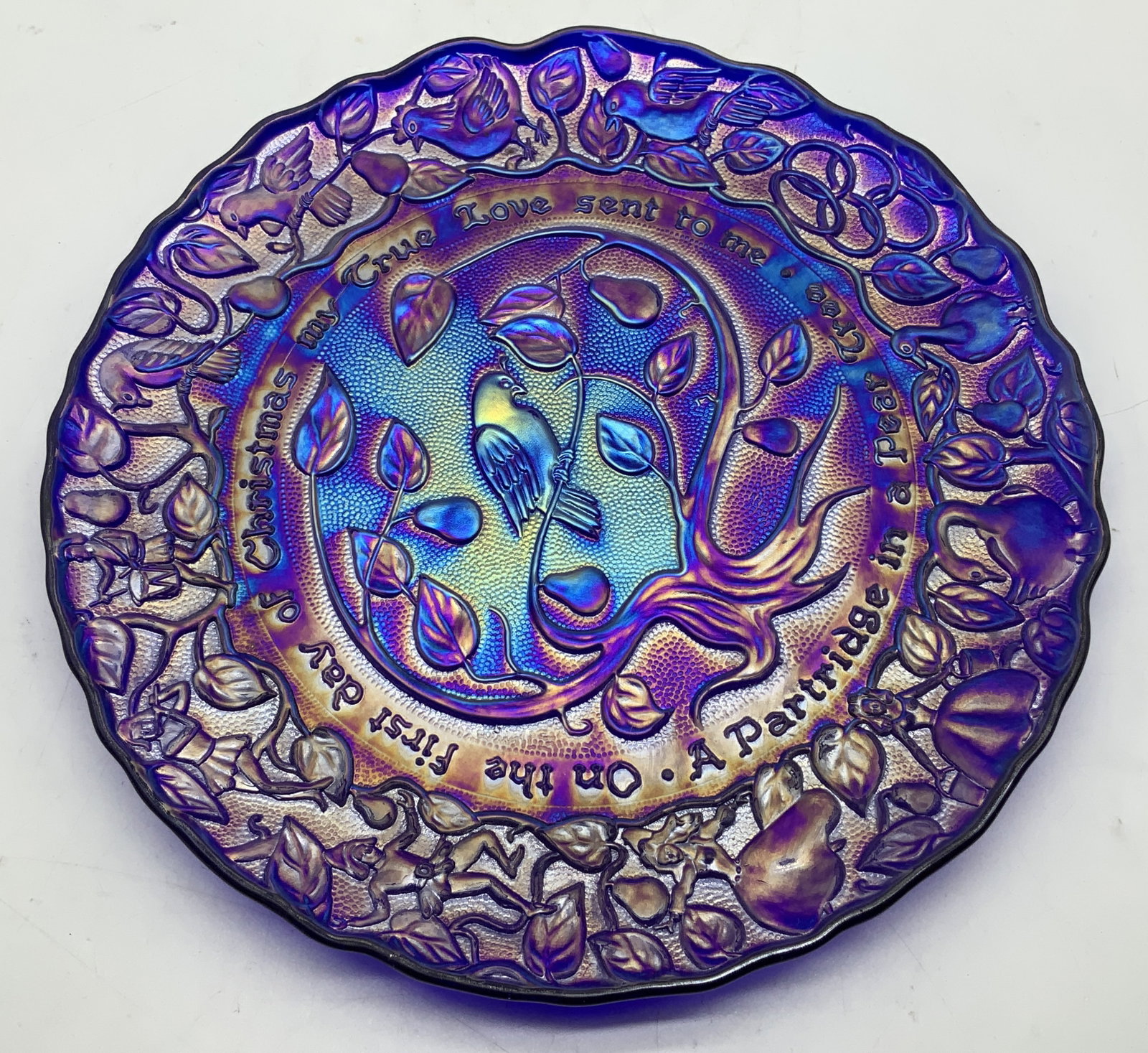 1970 Imperial Carnival Glass Christmas Plate: 1970 Imperial Glass Twelve Days of Christmas carnival glass plate featuring a Partridge in a Pear Tree design. Round shape. Iridescent blue. Signed & marked. Reads, THE TWELVE DAYS OF CHRISTMAS. PLATE