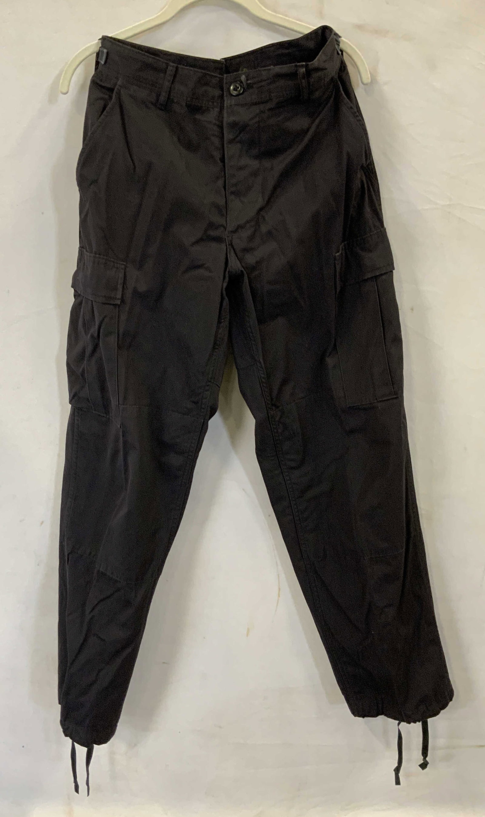 Black cargo pants with adjustable waist USA: Black cargo pants with adjustable waist. Made if a nylon cotton blend in USA Pants feature straps on the waist to adjust size anywhere from 27in- 31in. They also have adjustable drawstring cuffs and a