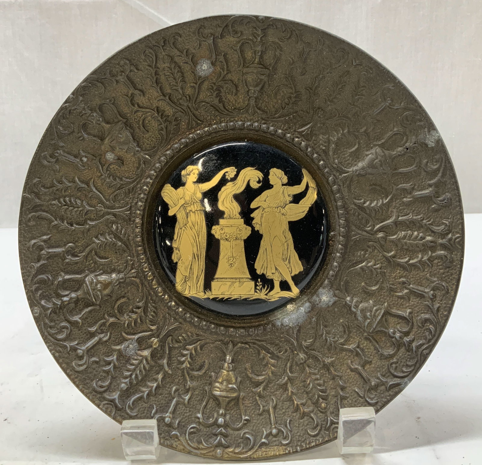 Vtg Classical Mythology Brass Deco Plate: Vintage brass decorative plate, featuring Roman figures in center. Raised urn & floral like motifs on border. Gilt accents. Piece has some weight. Round shape. Surface wear consistent to age, use & ex