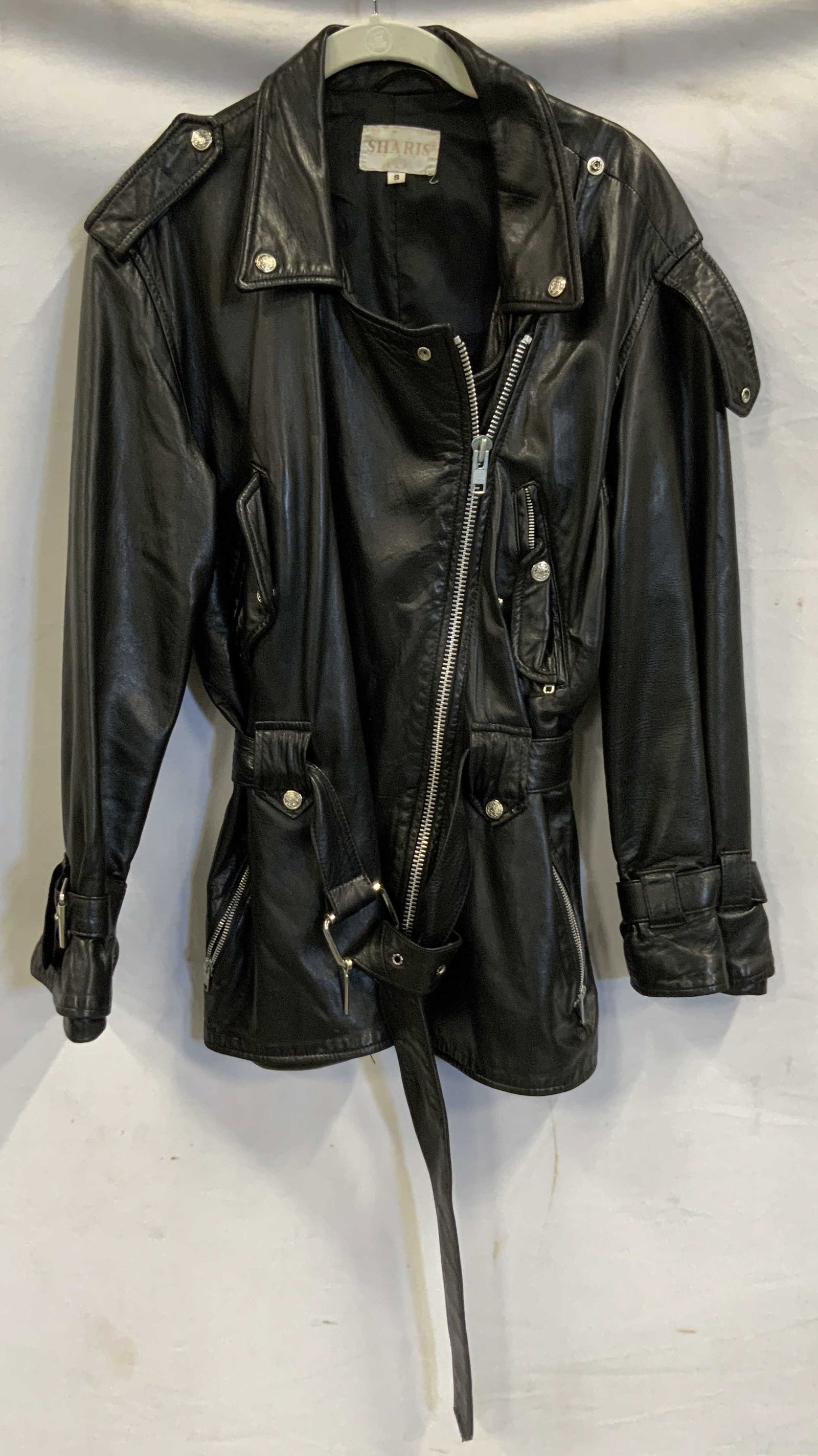 Sharis leather jacket with belt. USA: Sharis leather jacket with belt. Made in the USA. Jacket features snap pockets, belt loops, Collar , and shoulder detail. Belt around the waist and sleeve cuffs. Asymmetrical zipper closure. Size smal