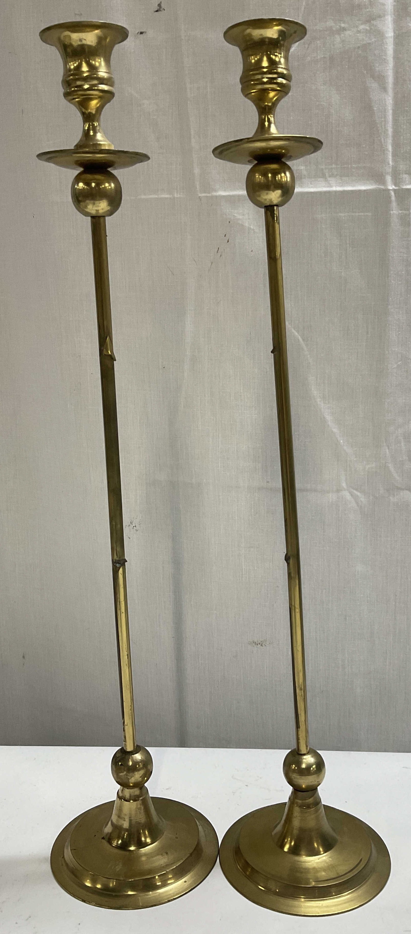VTG 19in Solid Brass Altar Candlesticks INDIA: Pair of Vintage Tall Handmade Solid Brass Altar Candlestick Holders. India. Slim Elongated Stems. Weighted Round Tiered Bases. Scratching, Peeling, Corrosion, and Tarnishing Present. One Needs Adjustm