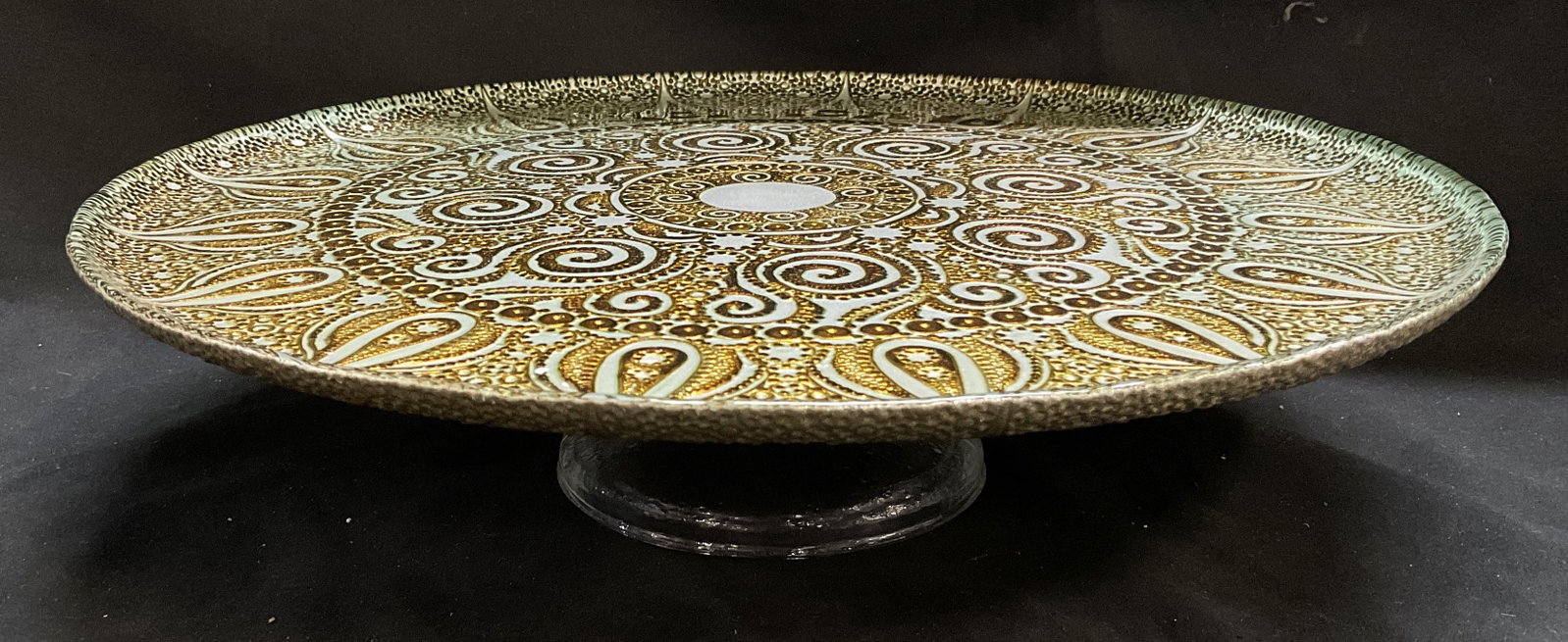VTG Metallic Glass w/ Gilt Mandala Cake Stand: Vintage Cake Stand. Gilt Mandala Design Over Silver-Toned Metallic Glass. Textured Gilt Design Underside. Clear Pedestal. Condition Consistent With Exposure. Measures app 4in H x 15in Diam. Vintage
