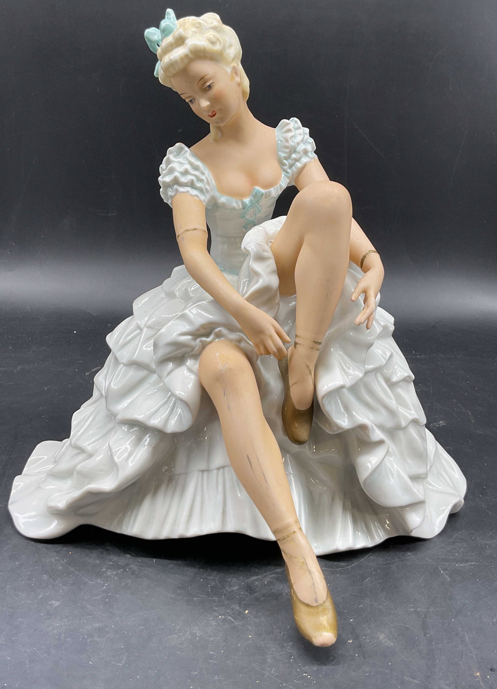 Schaubach Kunst Wallendorf Ballerina Fig Germany: Schaubach Kunst Wallendorf porcelain ballerina figure. Marked on underside, made in Germany. Seated ballerina figure in a ruffled rococo style dress tying her pointe shoe. Varying colors and hand pain