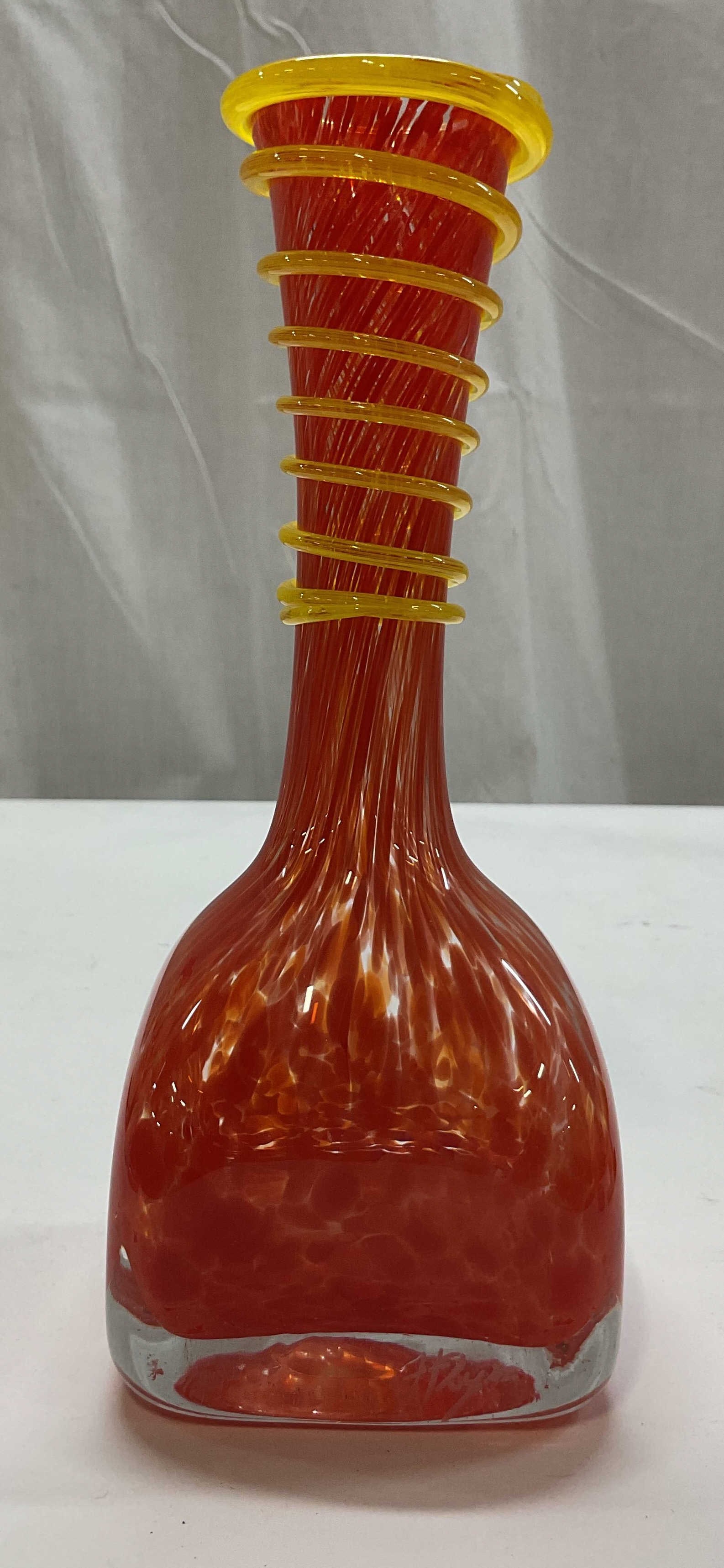 SGND Sabina Rymanow Orange Art Glass Vase: Signed Sabina Rymanow hand blown orange art glass vase. Signed on surface. Square shaped base with narrow neck. Abstract orange design. Applied yellow spiral coil around the neck and rim. Measures app
