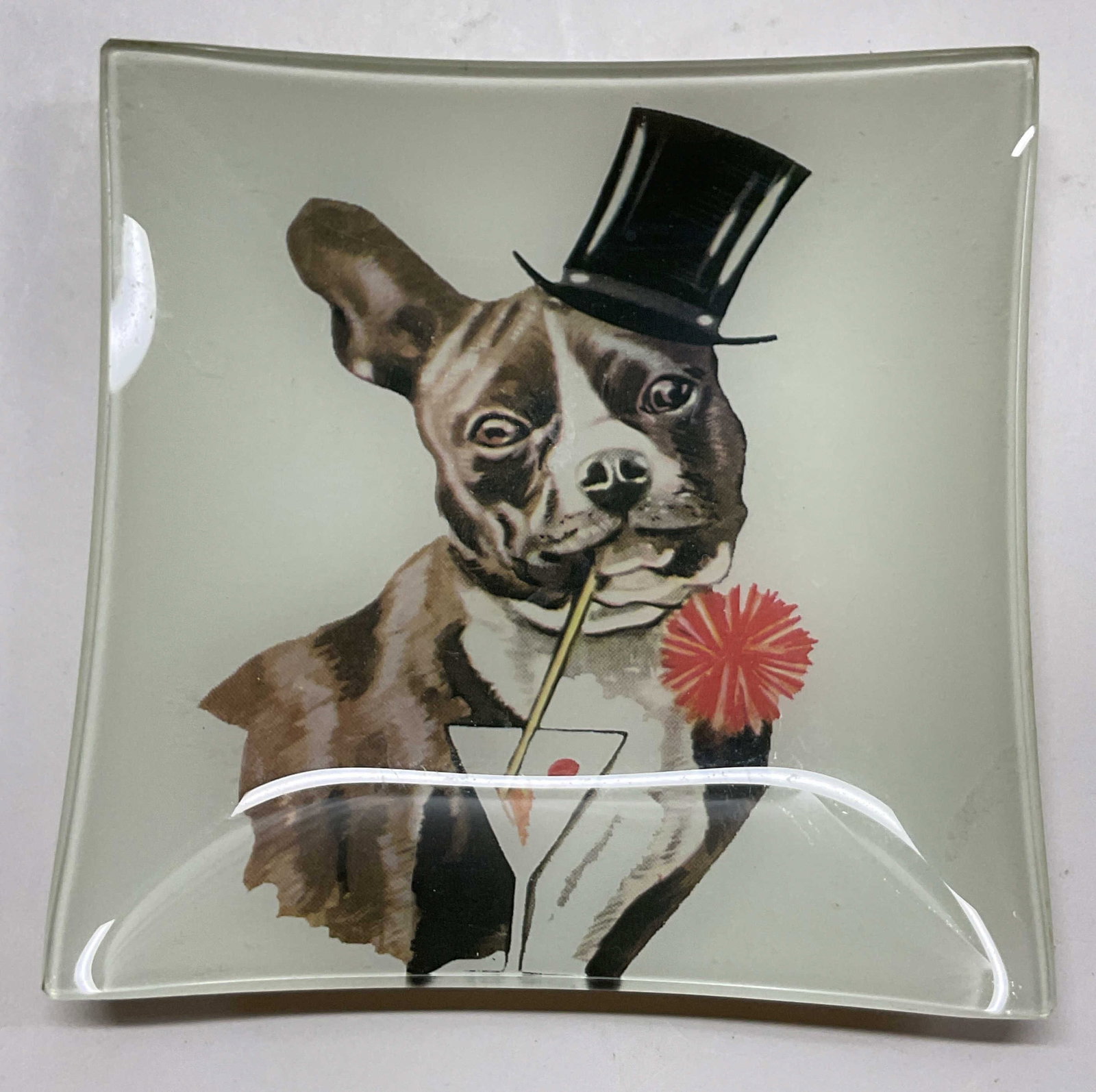 Vintage Glass Boston Terrier Trinket Dish: Vintage glass Boston Terrier trinket dish. Square shaped. Features imagery of a Boston Terrier wearing a top hat and drinking a martini, varying colors. Floral pattern on backside. Measures approx 6 x