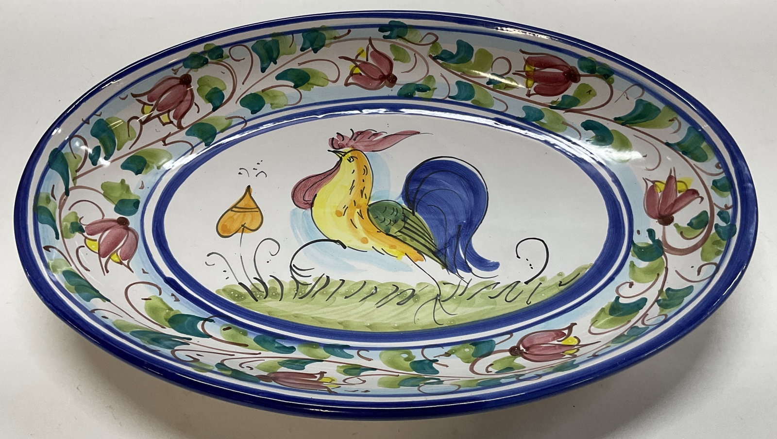 Vietri Hand Painted Ceramic Serving Platter Italy: Vietri hand painted ceramic serving platter. Marked on underside, made in Italy. Hook on underside for hanging. Blue trim. Oval shaped. Central rooster figure. Hand painted floral leaf and scroll moti