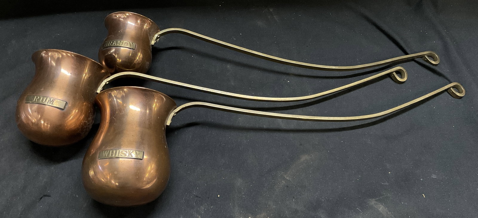 St3 VTG British Tavern Measuring Ladles: Set of 3 Vintage British Tavern Measuring Ladles. Copper Cups with Brass Handles and Plaques. Plaques Read Whisky, Rum, Brandy. Tarnishing Present. Various Sizes. Largest Measures app 4.5in H x 16.5in