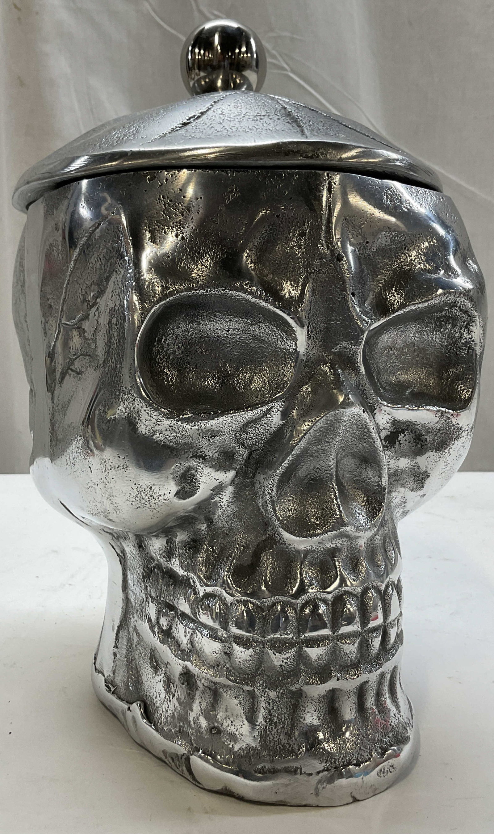 Vintage Metal Skull Head Lidded Cookie Jar India: Vintage metal skull head lidded cookie jar. Made in India. Detailed skull head. Comes with lid and ball finial. Inside compartment. Measures approx 6 x 7 x 11 inches. Scratching. Cookie jar, skull hea