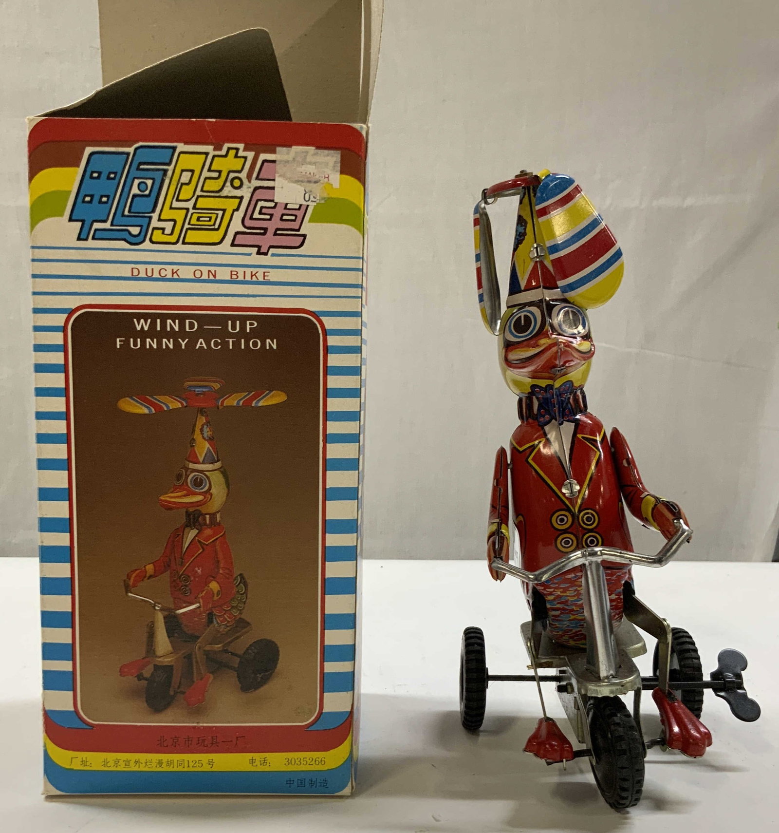 Vntg Duck on Bike Tin litho toy 1970s: Vintage Duck on Bike Tin litho toy from the 1970s. Made by the Beijing No. 1 toy factory. Mechanical clockwork tin toy featuring a dapper duck in a red jacket riding a triple with a propeller hat. Toy