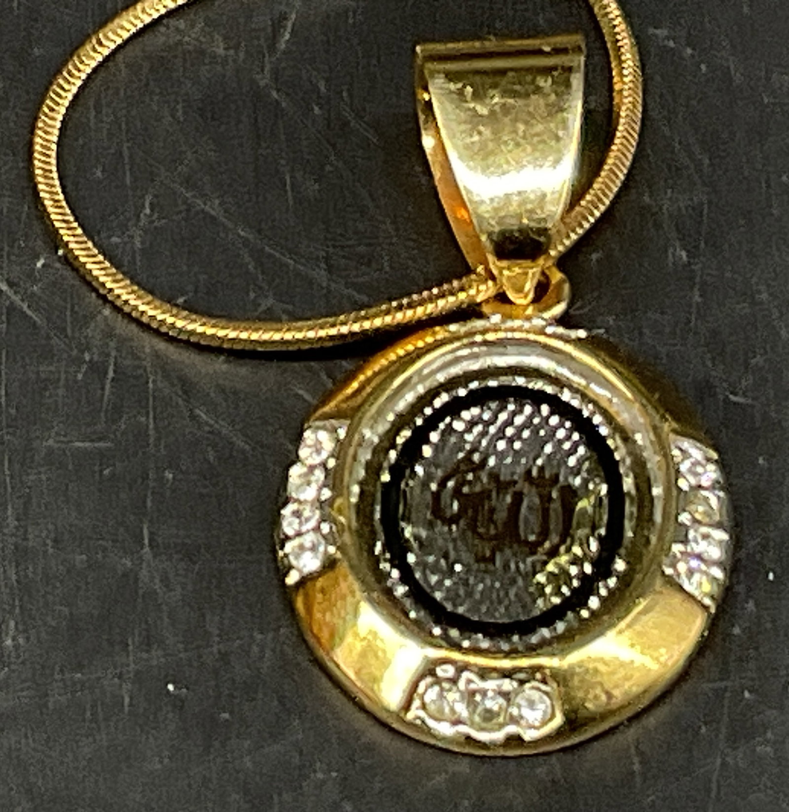 Gold-Toned Islamic Religious Pendant Necklace: Gold-Toned Islamic Religious Pendant Necklace. Possibly Gold-Plated. Features the Word Allah Written in Traditional Arabic Calligraphy in a Circular Frame with Silver-Toned Backing. Rhinestone Accents