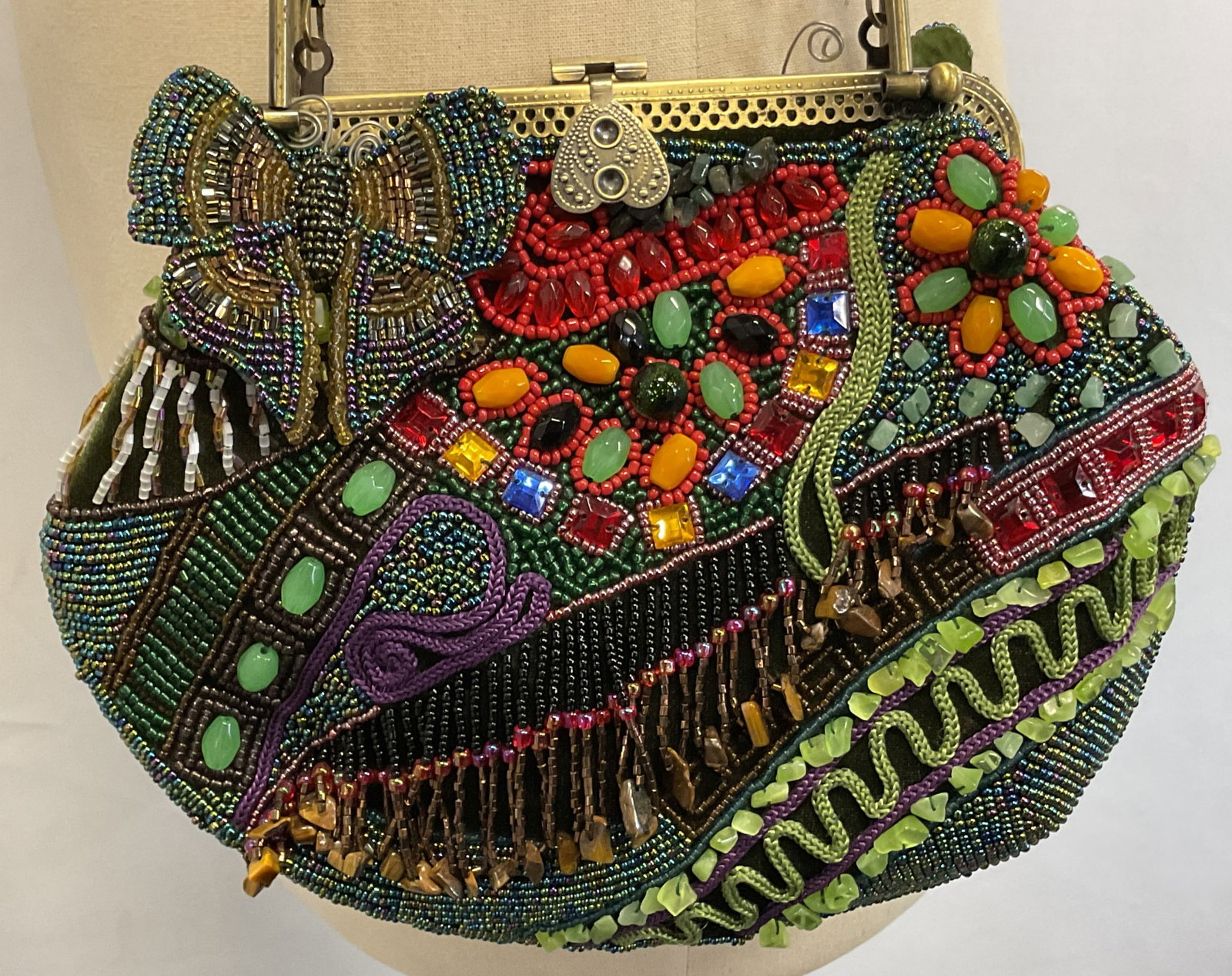 Vintage Beaded Silk Evening Bag: Vintage beaded silk evening bag. Green background. Adorned with beads and rope accents. Beaded butterfly, scroll, floral motifs. Metal attached strap and handles. Ornate heart closure. Inside compartm