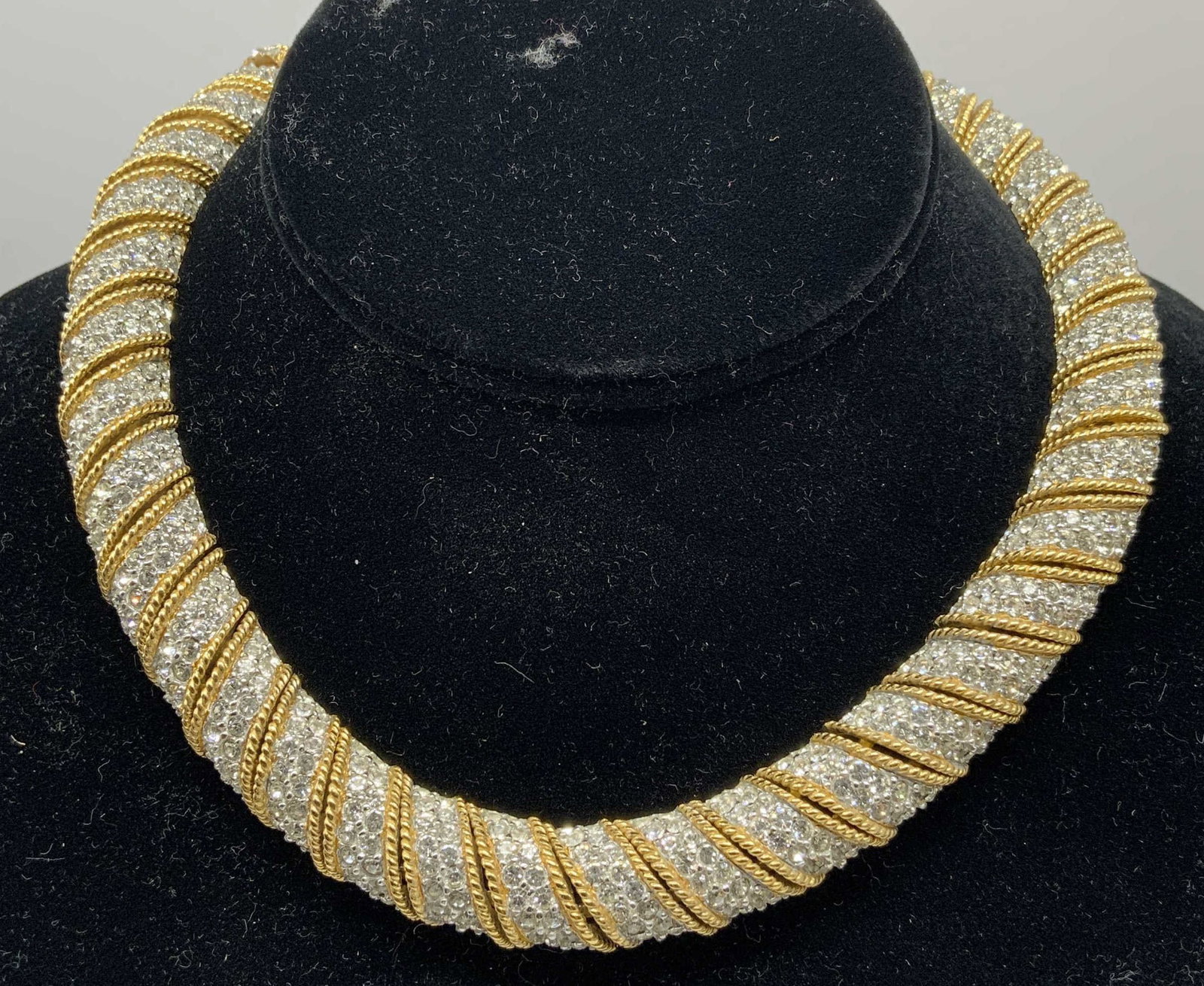 V. Ciner Gold-Tone Pave Rhinestone Collar Necklace: Vintage statement collar necklace by Ciner. Features heavy structured choker silhouette with alternating diagonal rows of clear pave set rhinestone bands separated by textured gold tone twisted rope a
