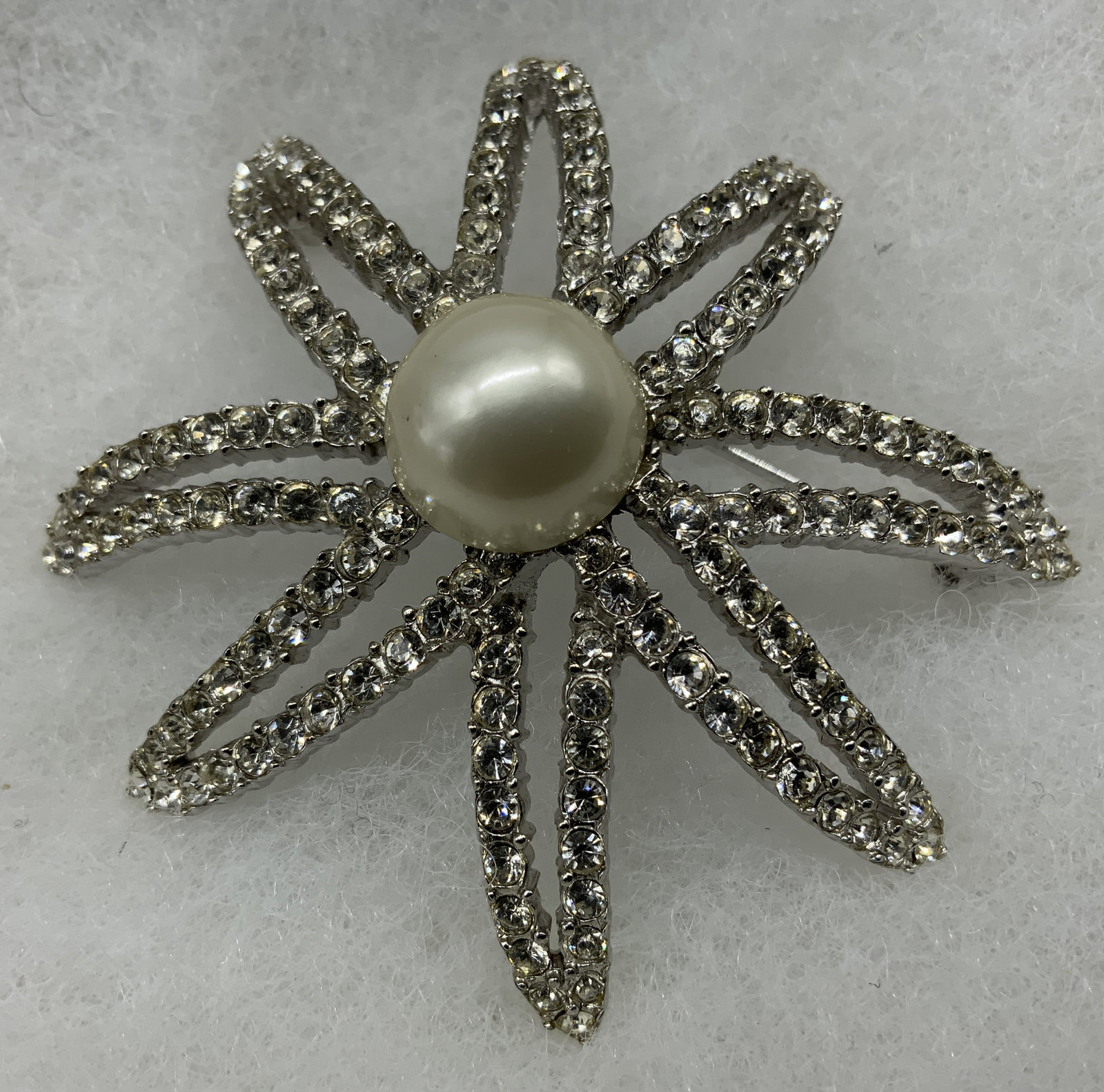 Vtg Ciner Rhinestone & Faux Pearl Brooch: Vintage circa 1980s Ciner statement starburst flower brooch/pin. Silver plated base metal, clear rhinestones, faux pearl. Designed either openwork multi tiered layout, eight sweeping looped petals ful