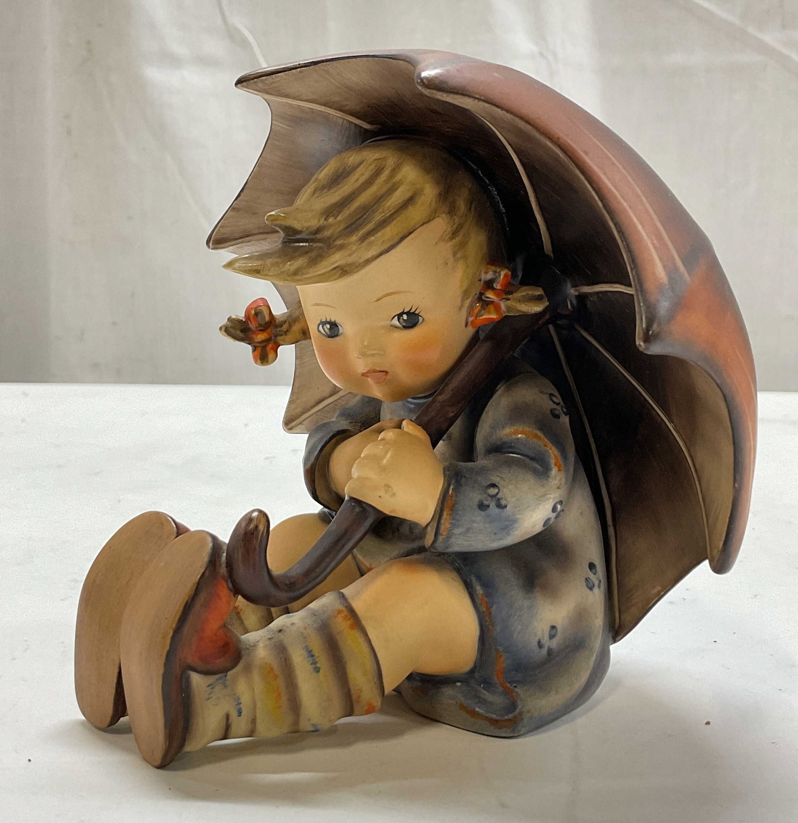 Hummel Goebel Porcelain Umbrella Girl Fig Germany: Hummel Goebel porcelain Umbrella Girl figure. Marked on underside, reads By W Goebel W Germany. Surface is signed. Depicts a young girl in a floral dress holding onto an oversize umbrella while seated
