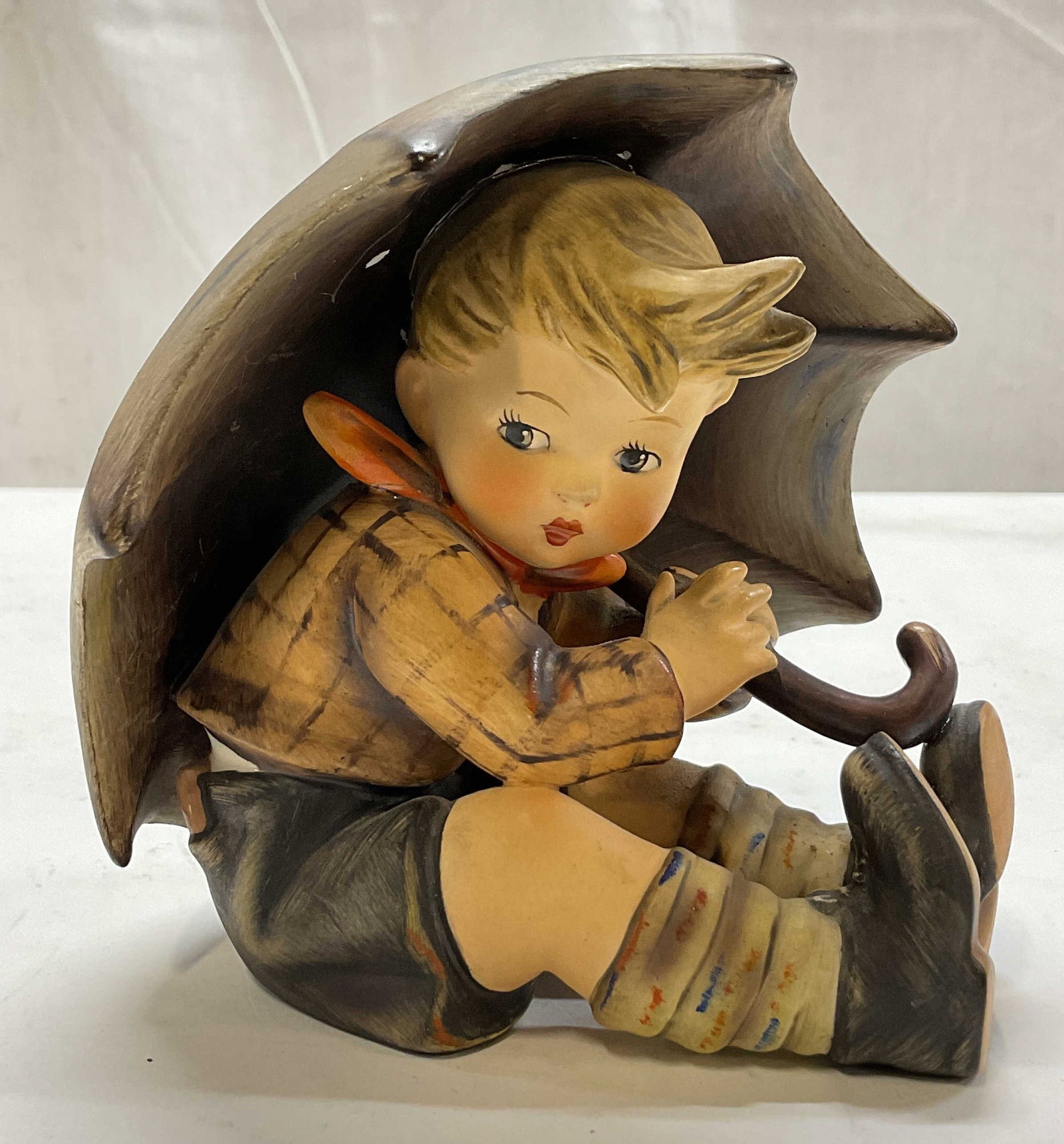 Hummel Goebel Porcelain Umbrella Boy Fig Germany: Hummel Goebel porcelain Umbrella Boy figure. Marked on underside, reads By W Goebel W Germany. Surface is signed. Depicts a young boy in a checkered jacket and brown shorts holding onto an oversize um