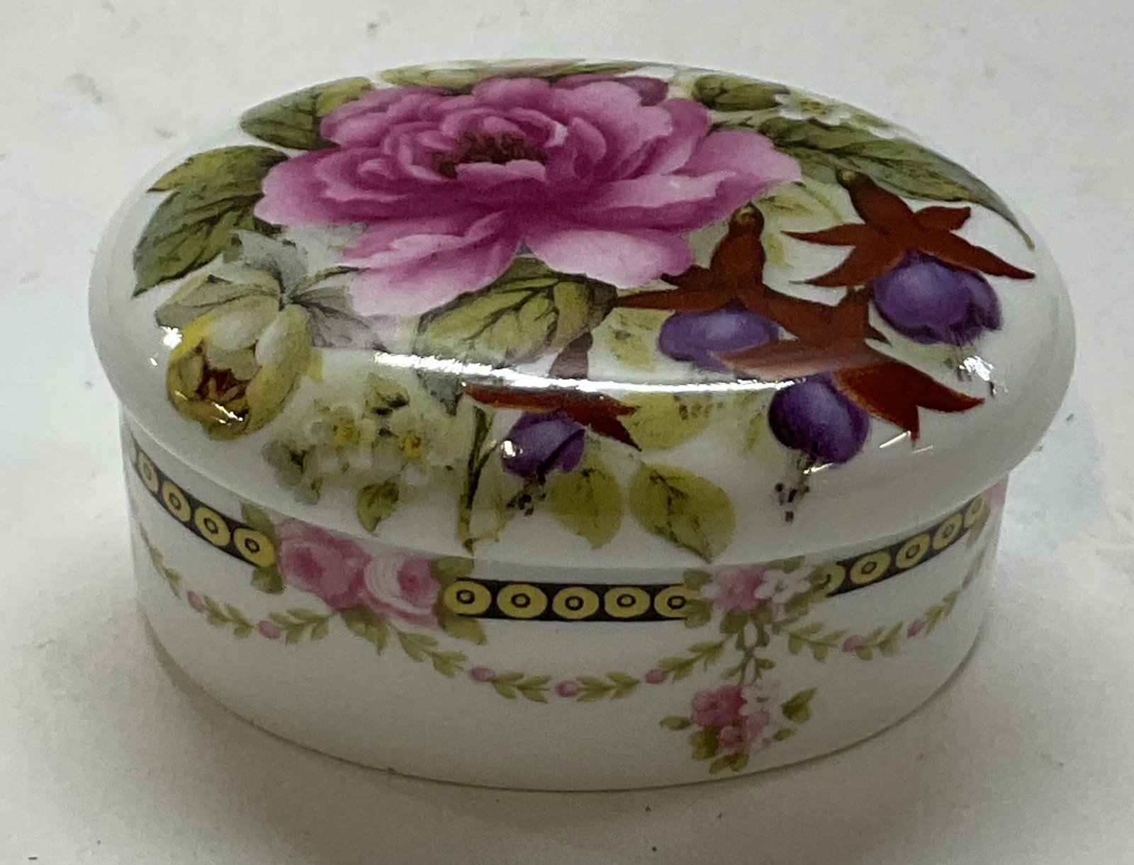 Crownford Giftware Bone China Pill Box England: Crownford Giftware bone china lidded pill box. Marked on underside, reads Fine Bone China Made In England. Oval shaped box. Floral and geometric motifs in varying colors. Measures approx 1.5 x 2 x 1 i