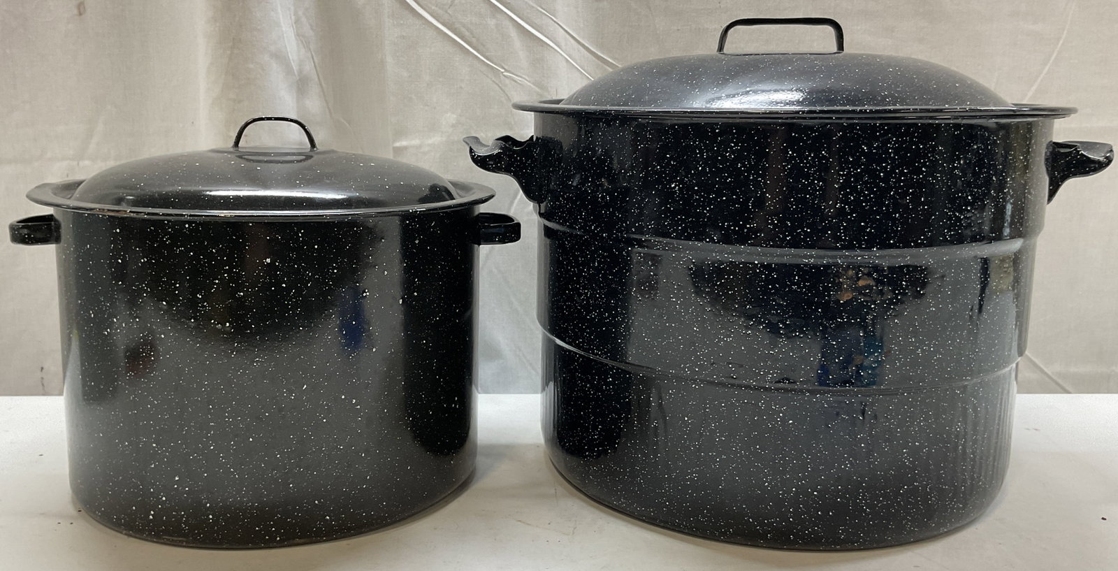 Lot 2 Vtg Black Enamelware Canning Pots W Lid: Lot of 2 vintage black enamelware canning pots. Both come with lids and have side handles. White speckled design. Size vary. Largest measures ht approx 13 inches diam approx 17.5 inches. Scratching.