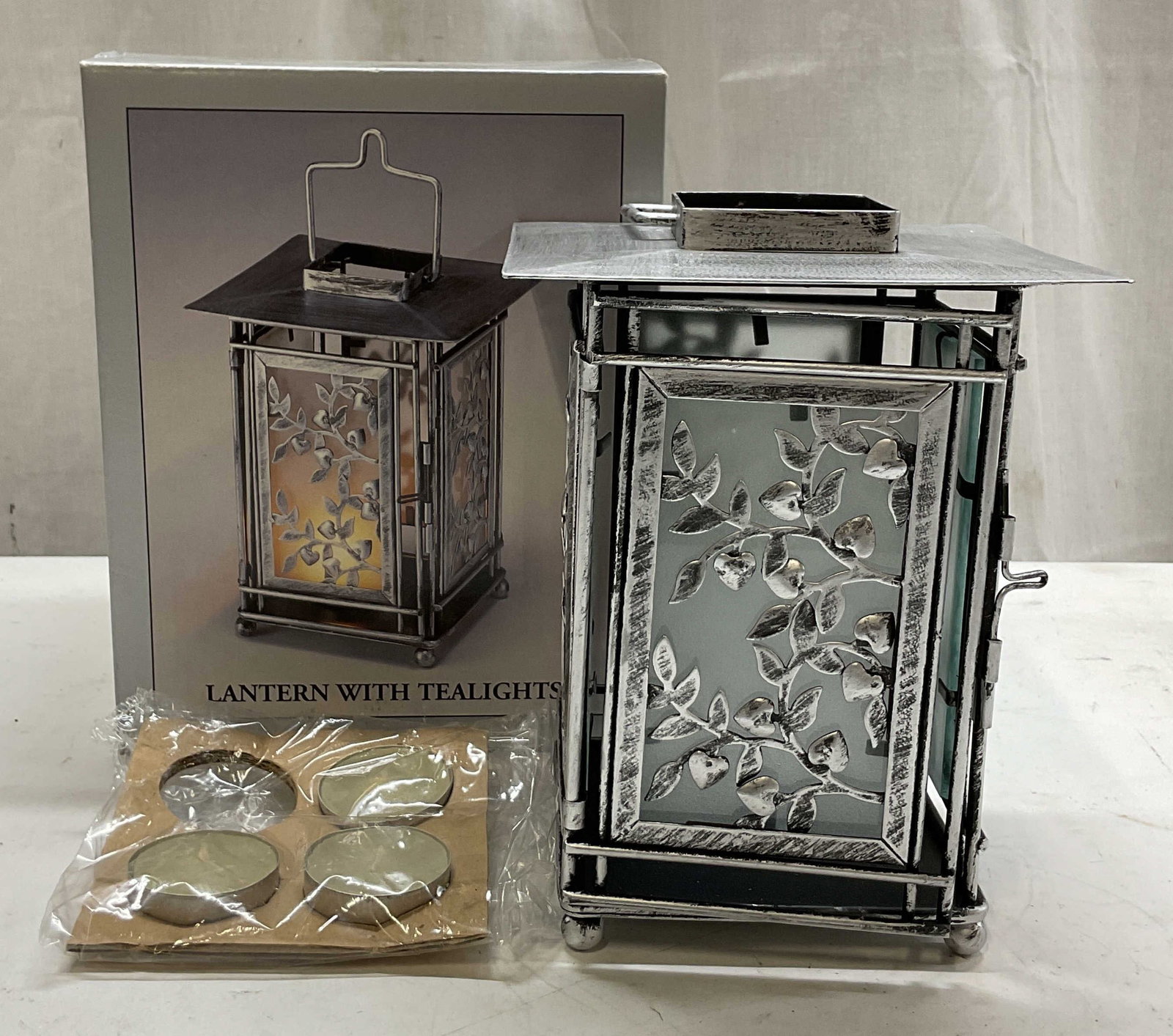 Silver Toned Metal & Glass Lantern W OG Box: Silver toned metal and glass lantern. Comes in original box with original packaging. Ball feet. Frosted glass panels. Delicate leaf and vine overlay. Distributed by JC Penney. lot includes 3
