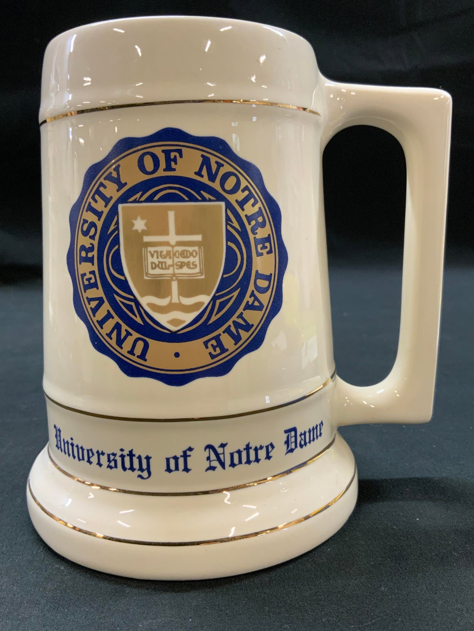Vtg University of Notre Dame Beer Stein Mug: Vintage University of Notre Dame Ceramic Beer Stein Mug. Circa 1980s. Styled in classic tankard silhouette. Body is finished in glossy cream glaze and accented by thin metallic gold gilded trim lines