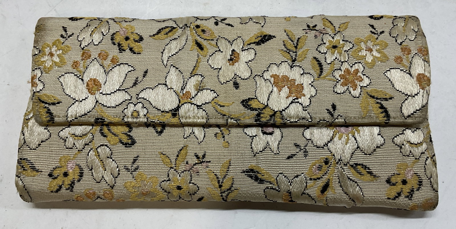 Vintage Beige Floral Brocade Clutch: Vintage beige floral brocade clutch. Rectangular shape. Fold over flap design with button closure. Woven floral motifs in varying colors. Interior compartments. Gold toned frame. Measures approx 4 x 8