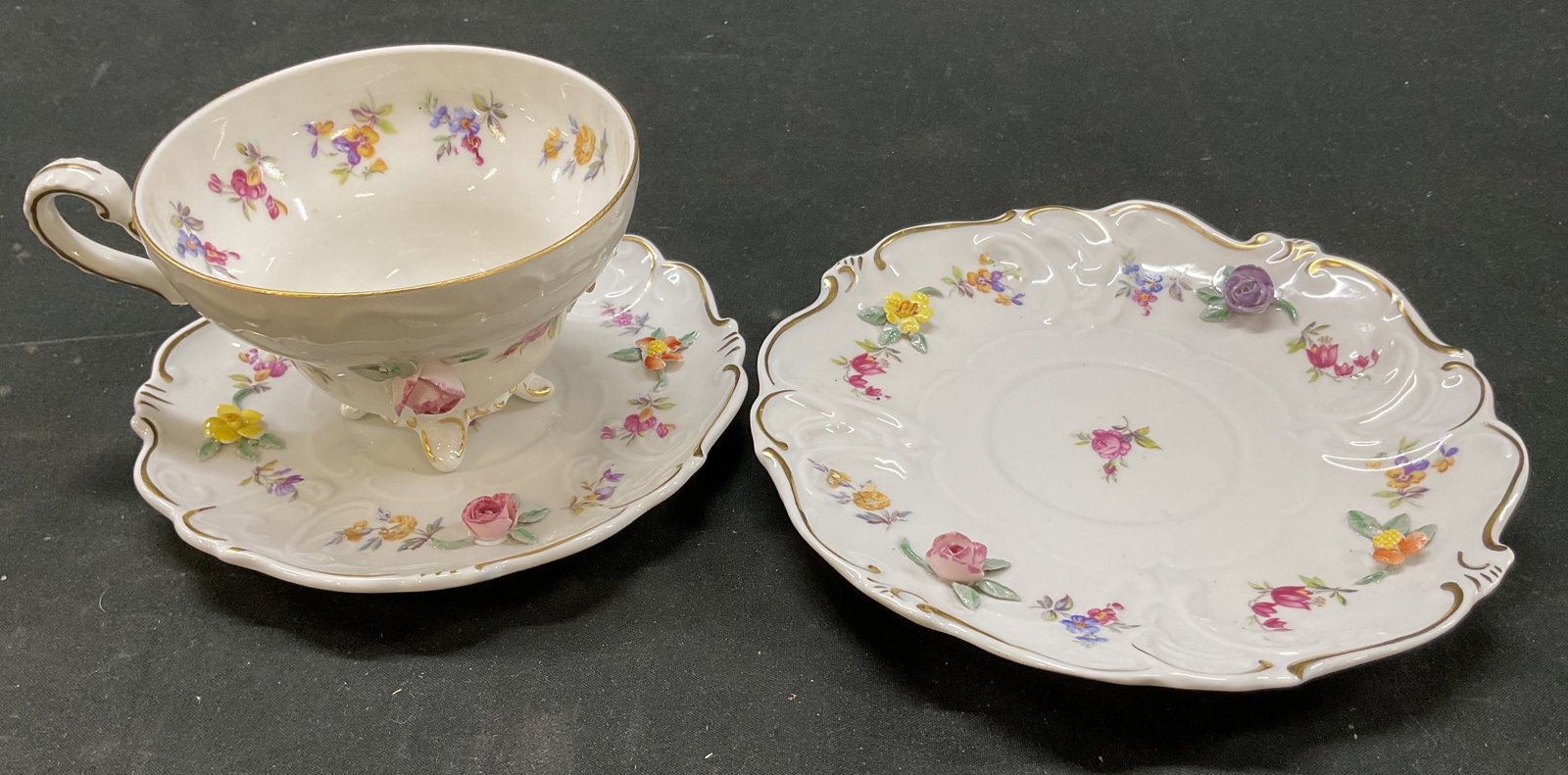 Set 3 Isco Teacup & Saucers Germany: Set of 3 Isco porcelain teacup and saucers. Marked on underside, reads Isco Germany. Two saucers and one footed teacup. Scalloped edge. Gilt border. Floral motifs in varying colors with raised