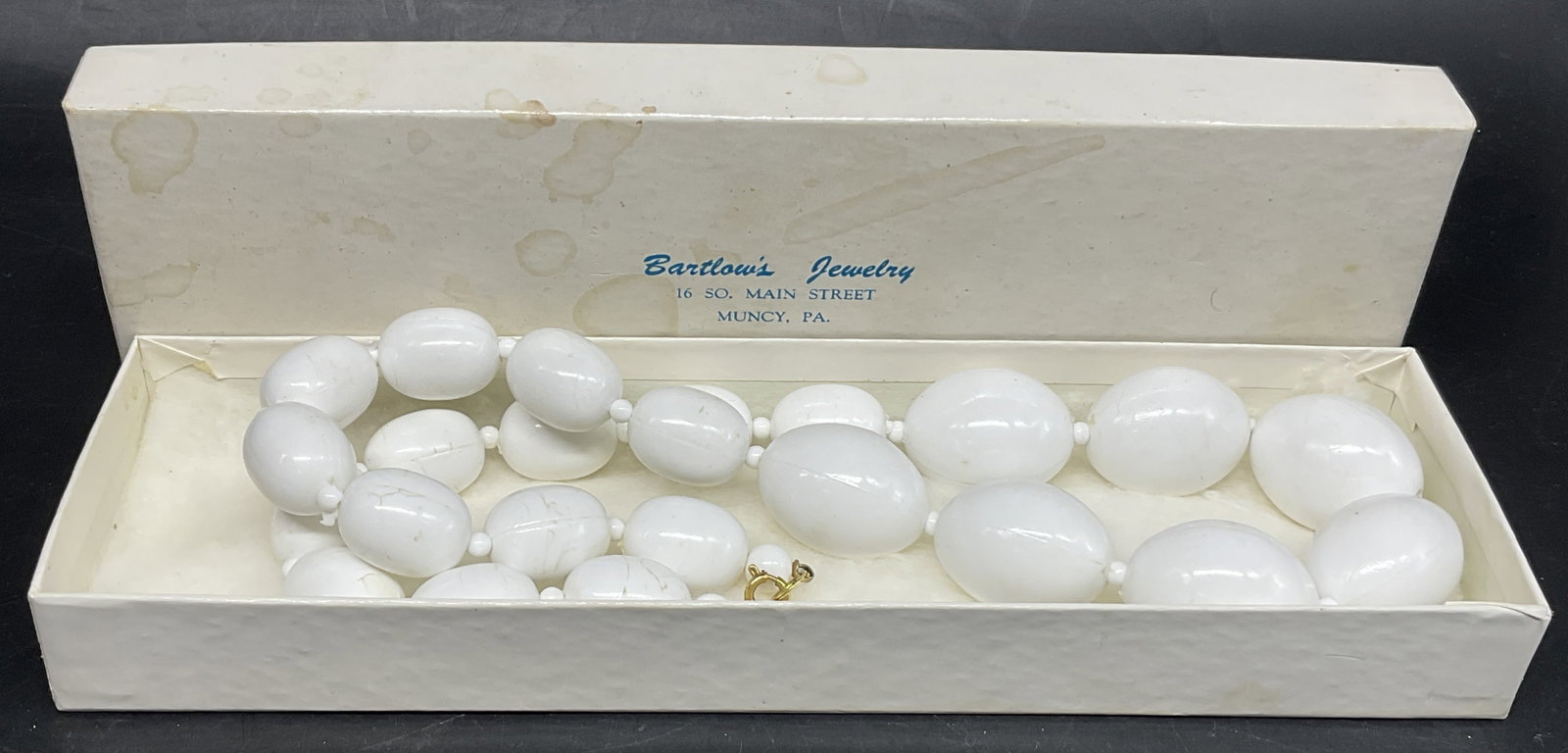 VTG Graduated White Lucite Beaded Necklace: Vintage Graduated White Lucite Beaded Necklace. Features Smooth Oval Beads That Gradually Increase in Size Toward the Center. Individually Separated by Small Spacer Beads. Comes with Bartlows Jewelry