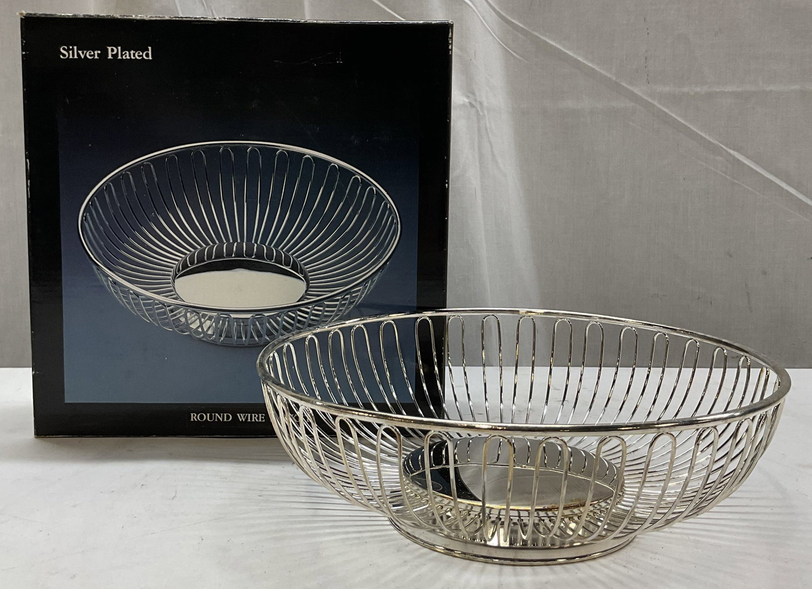 Caldor Inc Silver Plated Round Wire Basket W OB: Caldor Inc silver plated round wire basket. Comes in original box. Round basket with open frame design. Short pedestal base. Measures ht approx 3 inches diam approx 10 inches. Some wear to surface. Ro