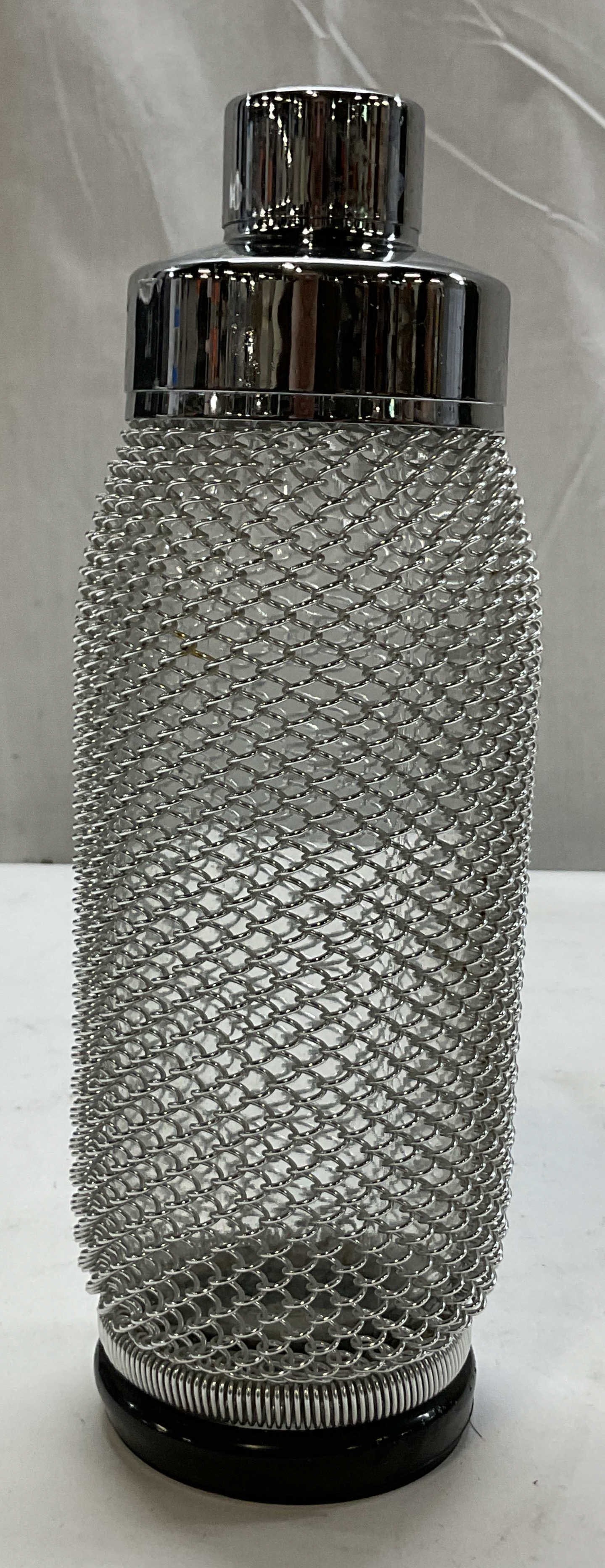 Merkuria Kovocas MCM Glass Cocktail Shaker: Merkuria Kovocas mid century modern glass cocktail shaker. Round black rubber base. Cylindrical glass bottle wrapped in a chrome style wire mesh. Silver toned cap. Measures ht approx 9.5 inches diam a