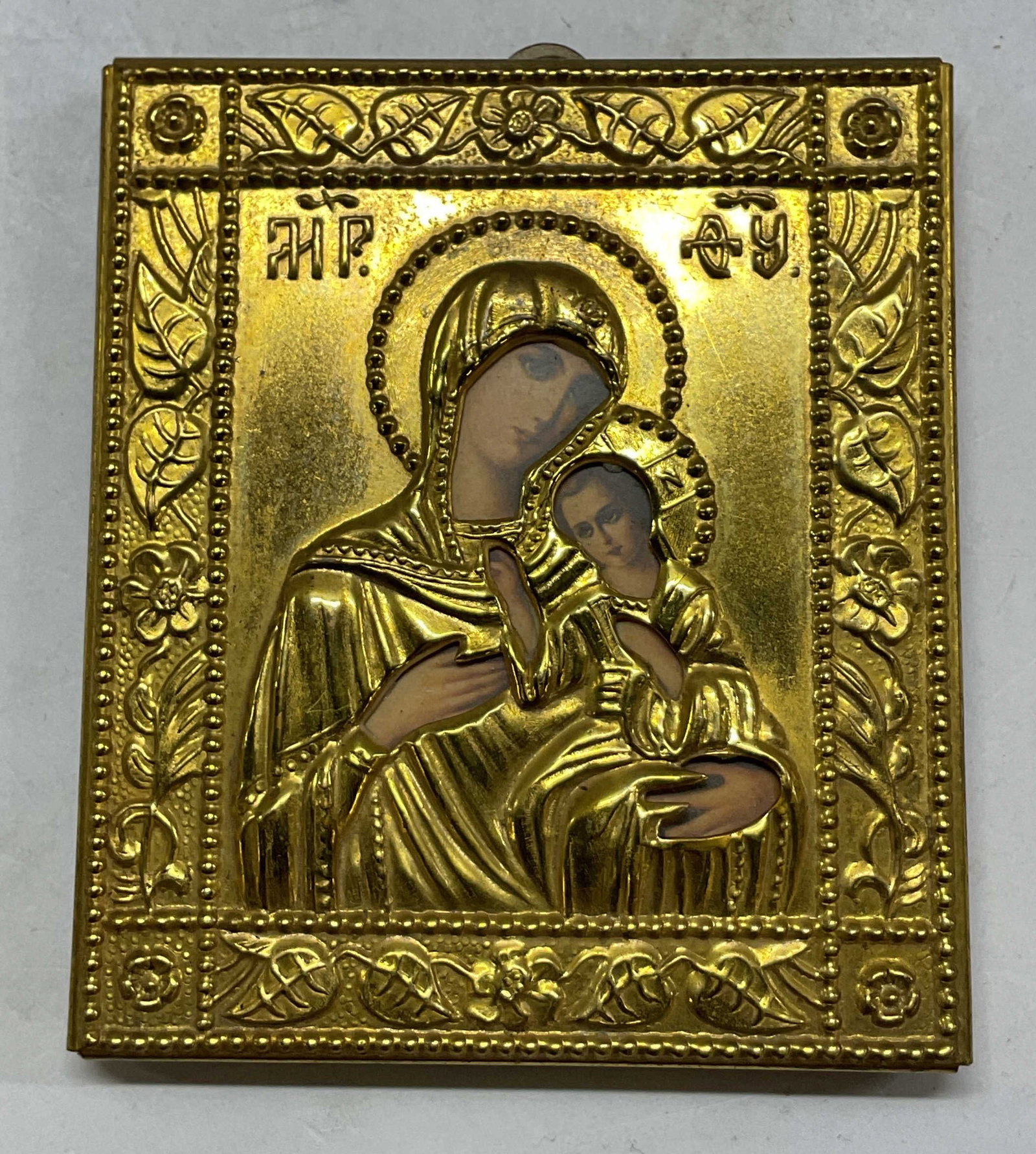 Vtg Traditional Gold Toned Religious Travel Icon: Vintage traditional gold toned religious travel icon. Square shaped. Features the Virgin Mary and Child. Greek lettering above. Embossed floral and beaded border. Small loop on top. Pink velvet back.