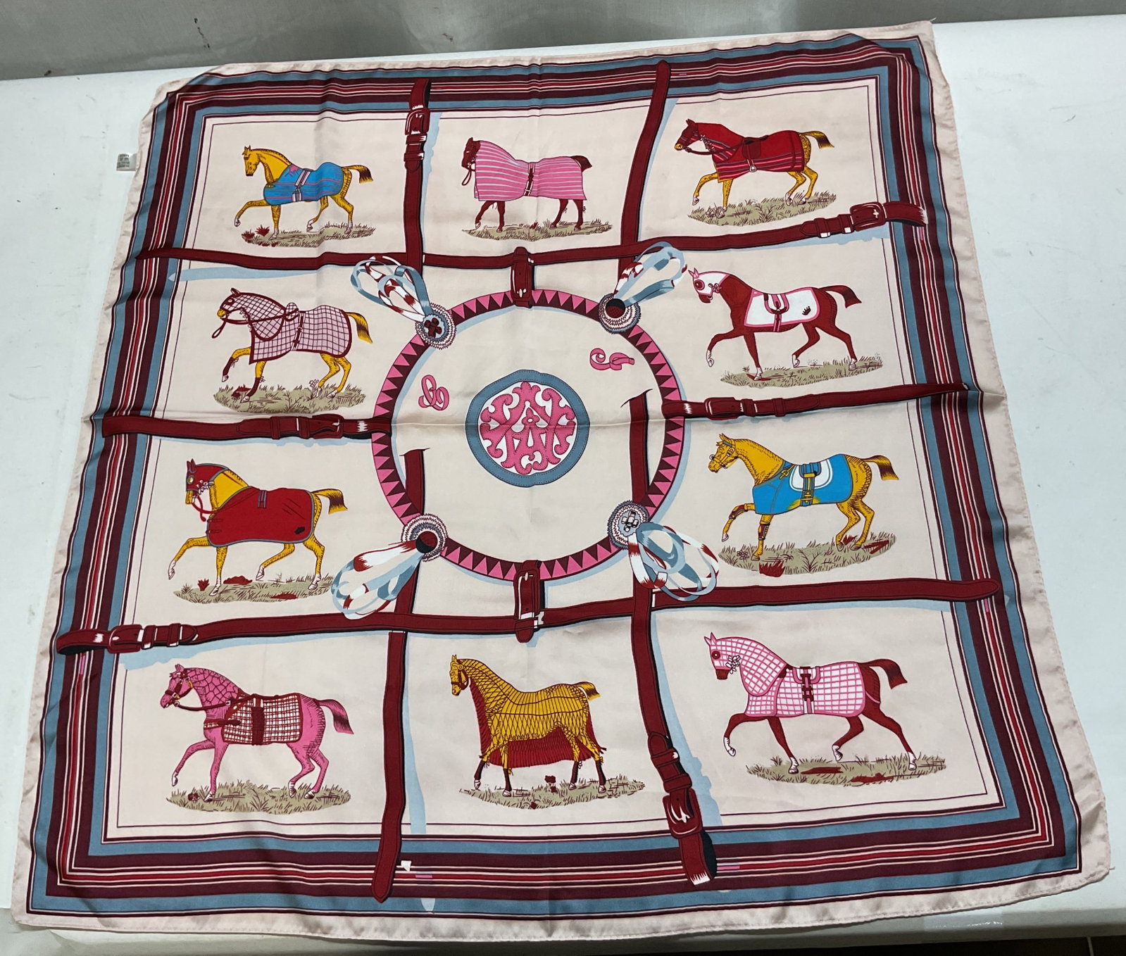Vintage Equestrian Themed Silk Scarf: Vintage Equestrian themed silk scarf. 70% viscose 30% silk. Varying colored and designed horses framed by leather straps. Central medallion design. Blue red and pink border. Measures approx 27.5 x 28 