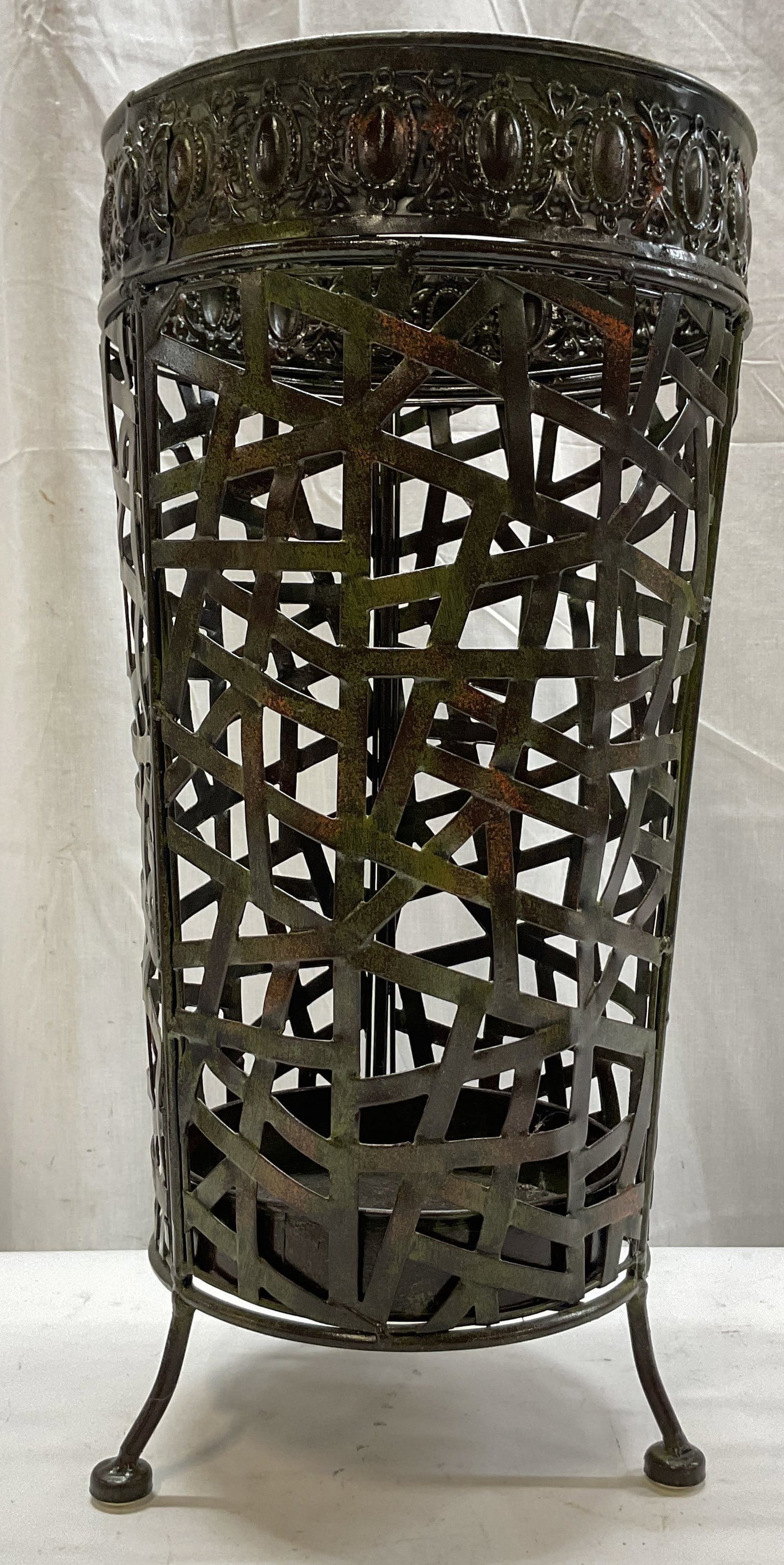 Vintage Metal Footed Decorative Umbrella Stand: Vintage metal footed decorative umbrella stand. Three curved legs with round feet. Tall cylindrical shape. Patinated. Abstract criss cross design on body. Ornate embossed scroll motif rim. Measures
