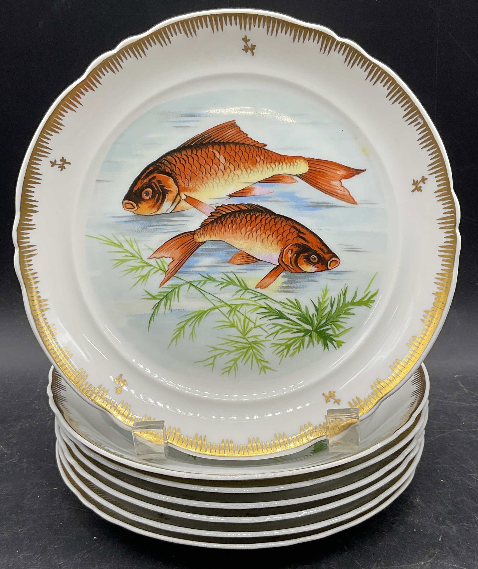 Set 7 Hand Painted Gilt Fish Porc Plates, France: Set of 7 porcelain plates. Hand painted fish motifs with gilt rims. Made in France. Measures approx. 7.5 inches wide. Some wear to all including scratching and loss to paint. Fish plates, porcelain