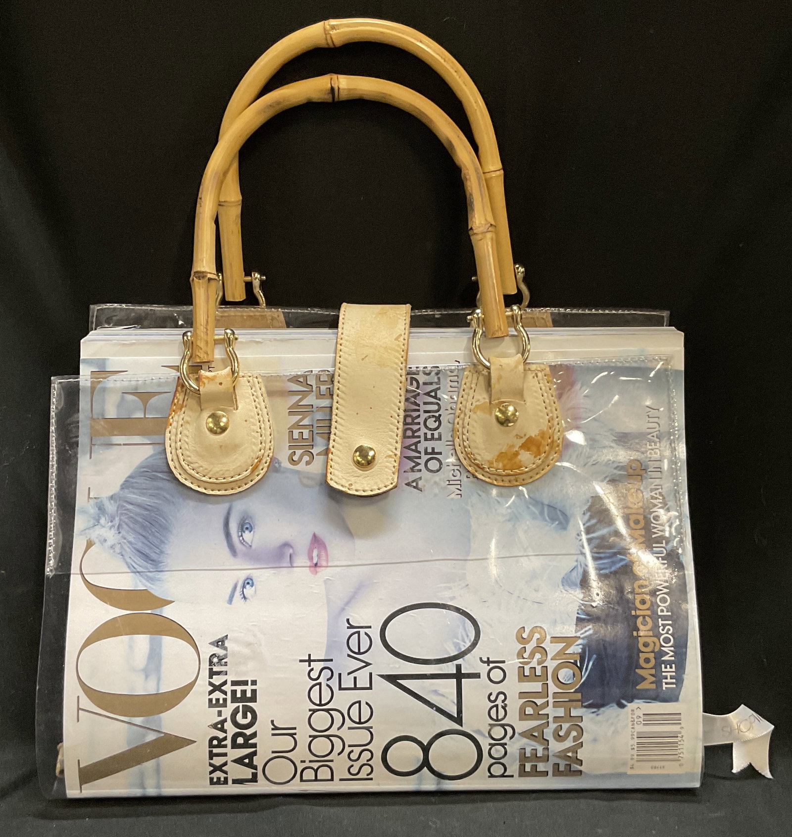 VTG Magazine Purse w/ 2007 Ed Vogue Mag: Vintage Magazine Purse with 2007 Edition of Vogue Magazine. Clear Vinyl with Leather and Bamboo Handles. Brass Hardware. Some Staining on Leather. Measures app 13.5in H x 11in L x 8.5in W. Vintage