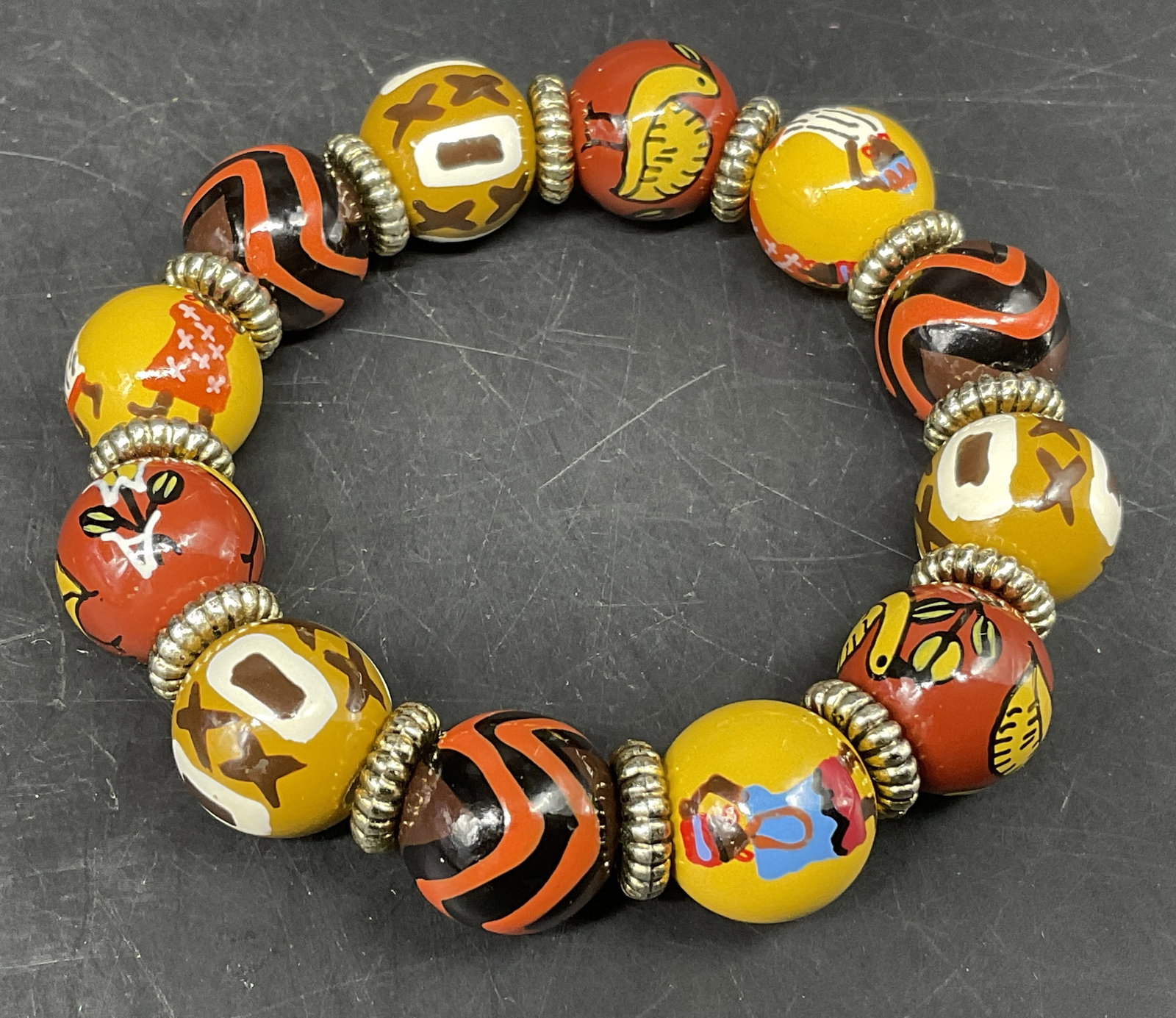 VTG-Style Artisan Hand-Painted Bead Bracelet: Vintage-Style Artisan Hand-Painted Bead Bracelet. Composite Material. African Folk Art Style Illustrations of Birds and Figures As Well As Geometric Shapes. Ribbed Silver-Toned Spacer Beads.