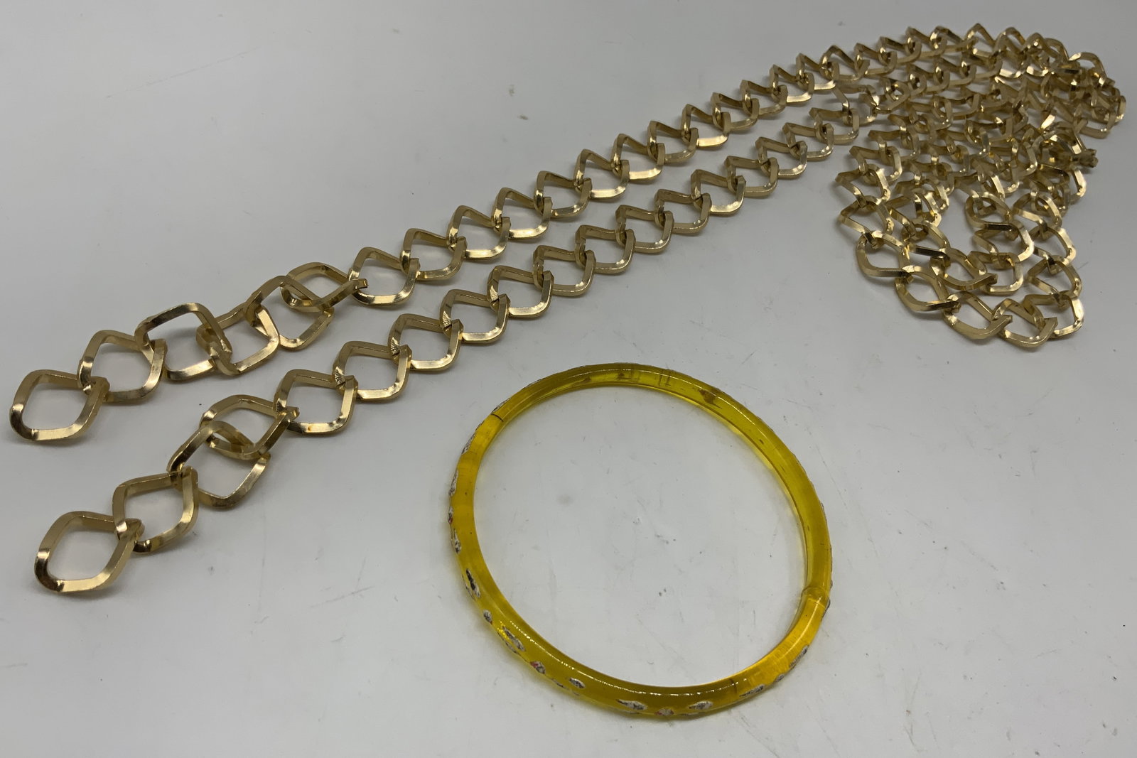 Vtg Gold Tone Chain Belt and Acrylic Bangle: Vintage Lot2 Gold tone chain belt and acrylic bangle. Long line waist belt constructed from polished gold tone metal. Features geometric openwork links in an interlocking diamond shape structure.