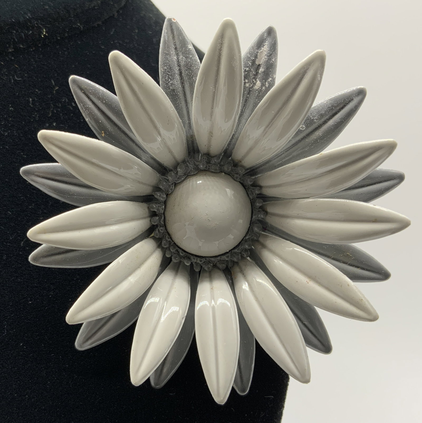 Vtg White+Grey Enamel Sunflower Brooch: Vintage costume jewelry brooch designed as dimensional flower. Layers of pointed metal petals coated in white and grey enamel finishes. Center of blossom holds circular white cabochon insert. Reverse 