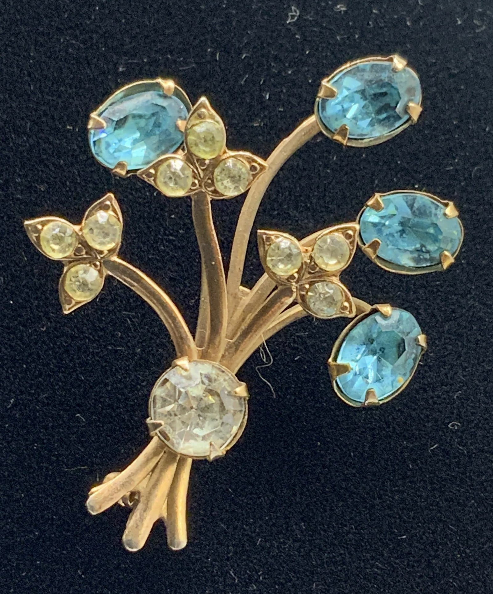 Vtg Rhinestone Floral Spray Brooch: Vintage Rhinestone Floral Spray Brooch. Gold tone costume jewelry wire stems gather at central wrapped base branching out to hold four prong set oval cut blue rhinestones. Rollover safety clasp on bac