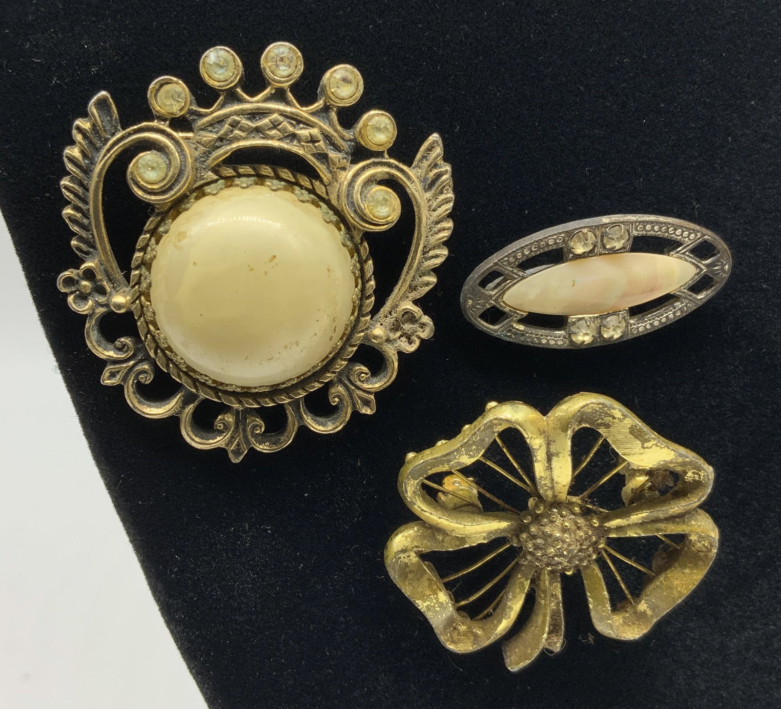 Vtg Lt3 Costume Jewelry Brooches: Vintage lot of 3 costume jewelry gold tone brooches. Includes: Large circular brooch- gold tone openwork structural piece featuring large cream dome cabochon. Border accented with scrolling filigree m