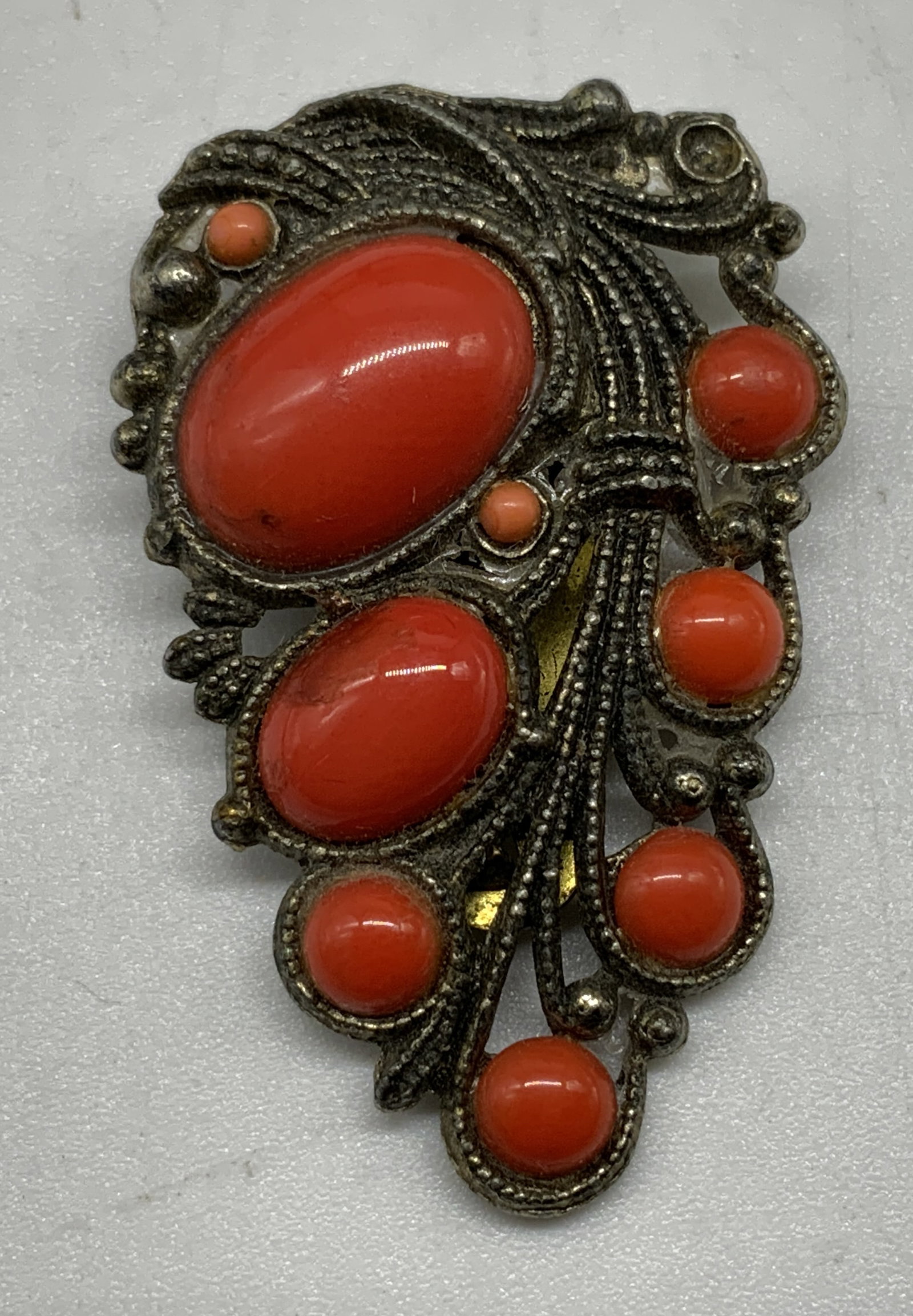 Vtg Faux Coral Silver Tone Dress Clip: Vintage costume jewelry dress clip fitted with a large triangular brass tone spring clip. Structure inset with multiple smooth orange red faux coral cabochons. Condition consistent with age and exposu