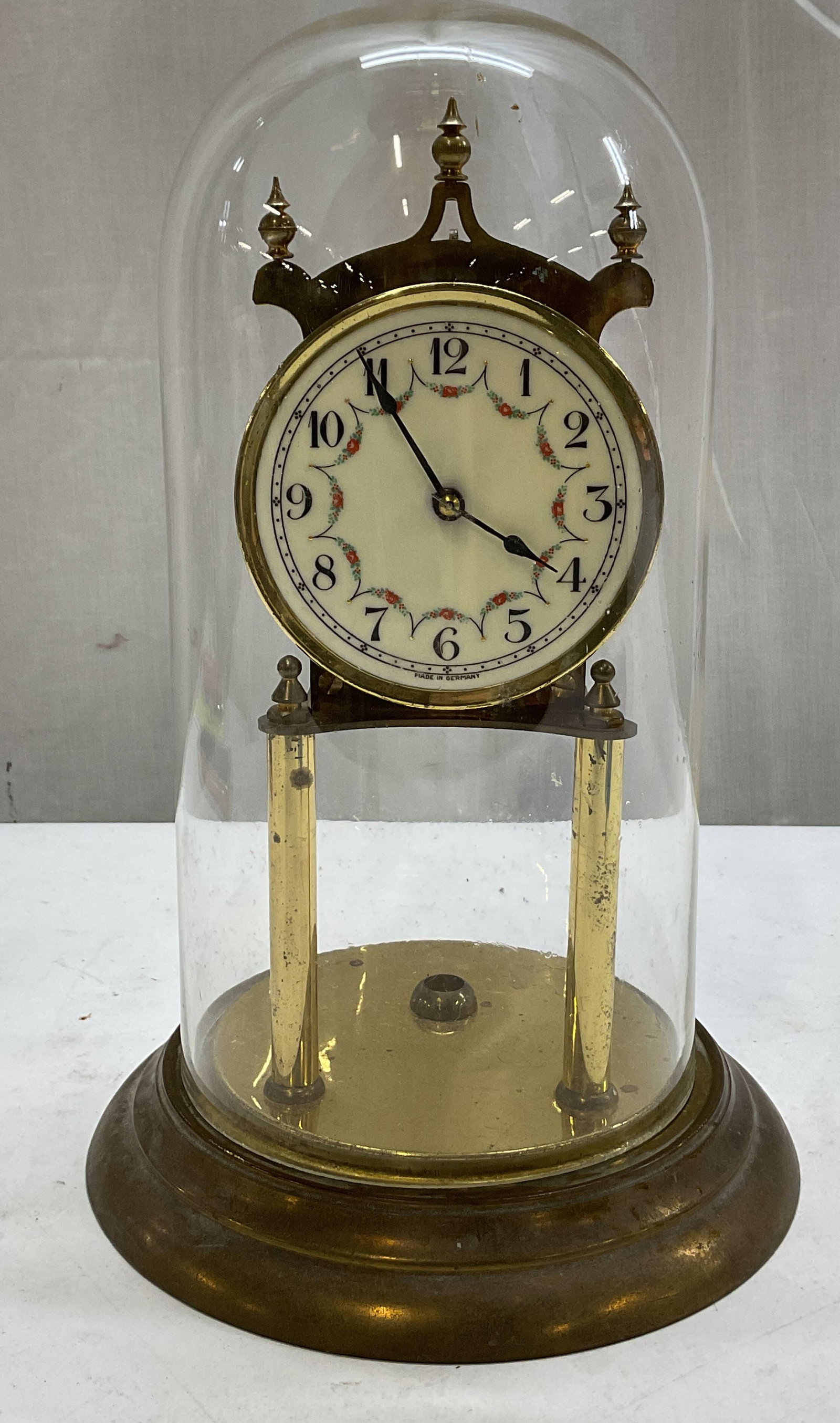 Kundo Kieninger & Obergfell Anniver Clock Germany: Kundo Kieninger & Obergfell 400 day mechanical anniversary clock. Marked made in Germany. Round wide base. Glass dome. Brass pillar dial face with varying colored floral motifs. Measures ht approx 12