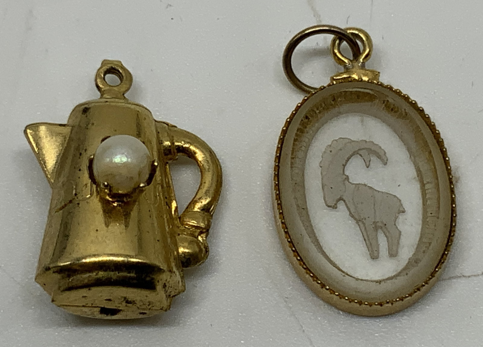 Vtg Lt2 Gold Tone Intaglio & Coffee Pot Charms: Vintage lot of 2 charms. Includes 1x oval intaglio charm, reverse carved acrylic panel with stylized animal profile. 1x coffee pot charm, three dimensional molded gold tone charm styled as coffee